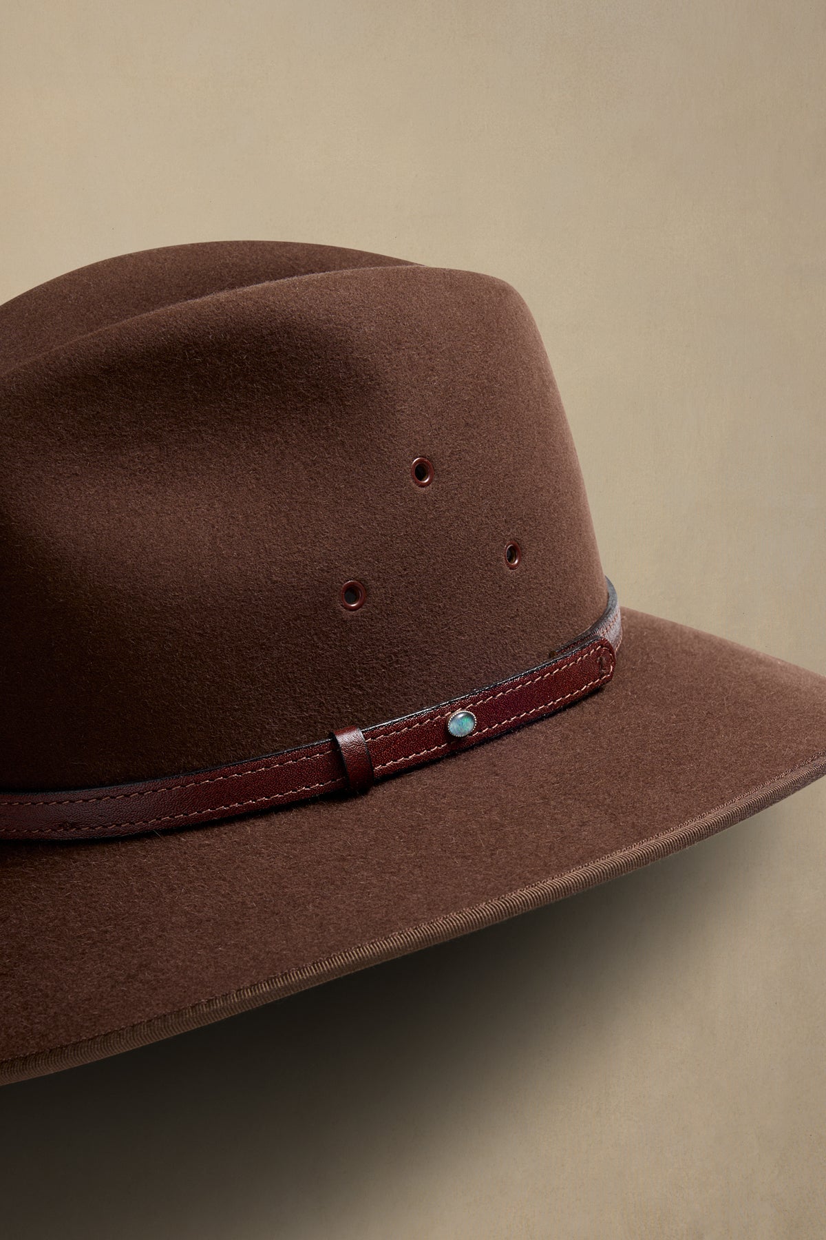 Brown fur felt cowboy hat with leather band and turquoise stone detail, angled side view against neutral background