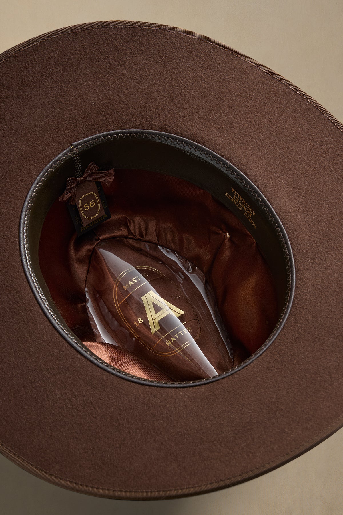 Brown felt Coober Pedy hat displayed inside open packaging, showing size 56 label and burgundy silk lining