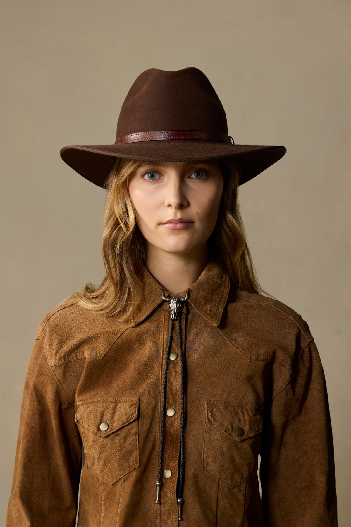 Brown felt cowboy hat with leather band on child wearing tan suede shirt against neutral background