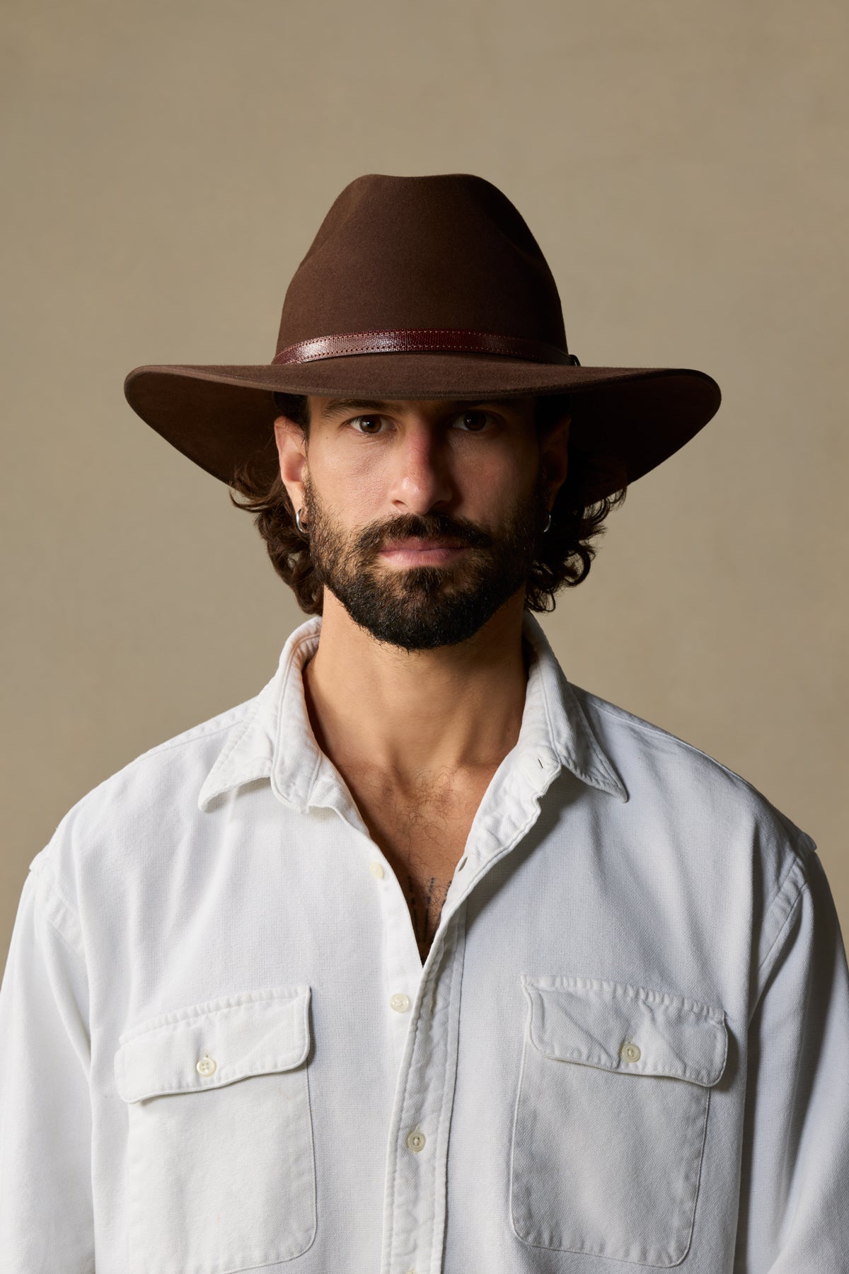 Brown felt Coober Pedy cowboy hat with leather band worn with cream button-up shirt on neutral background