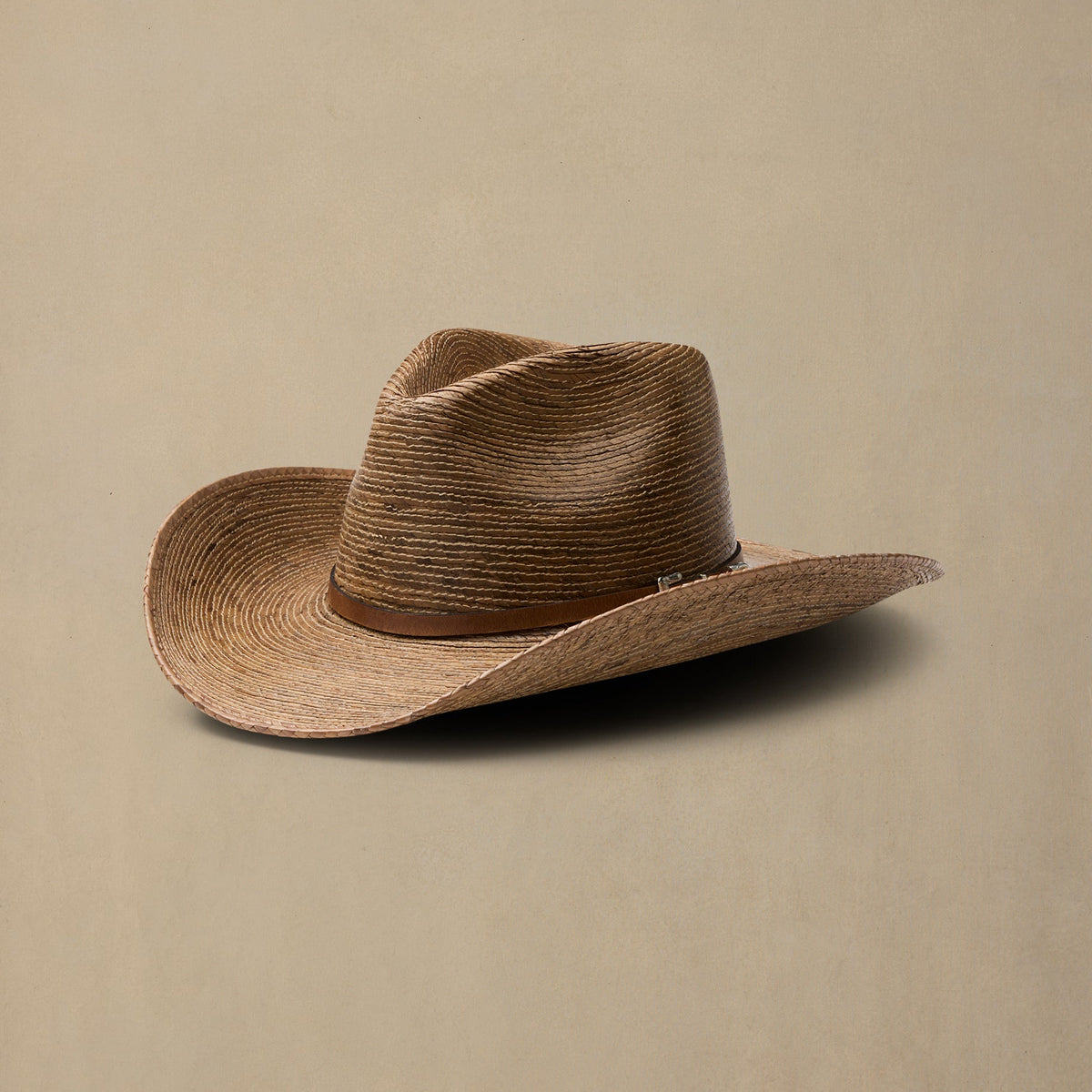 Tan woven straw cowboy hat with brown leather band on neutral beige background
