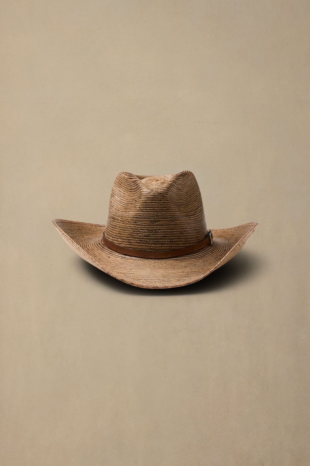 Tan woven straw cowboy hat with brown band on neutral beige background, front view