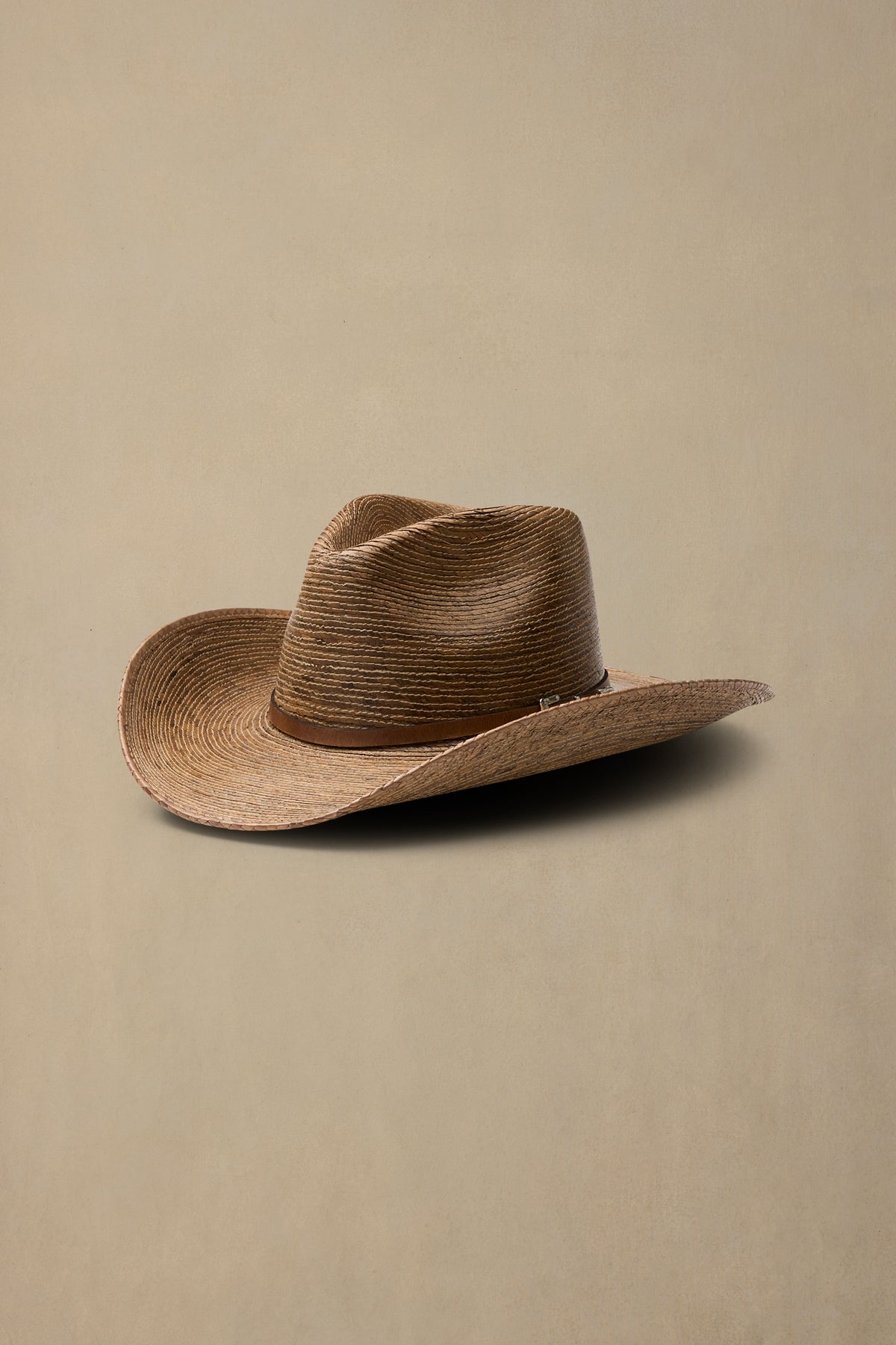 Tan woven straw cowboy hat with dark brown leather band on neutral beige background