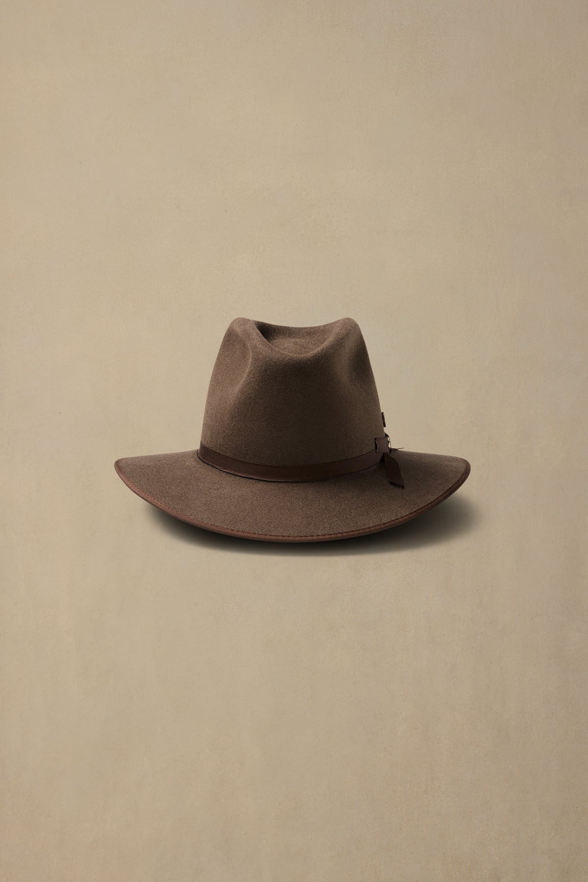 Mid brown fur felt cowboy hat with leather band on neutral beige background