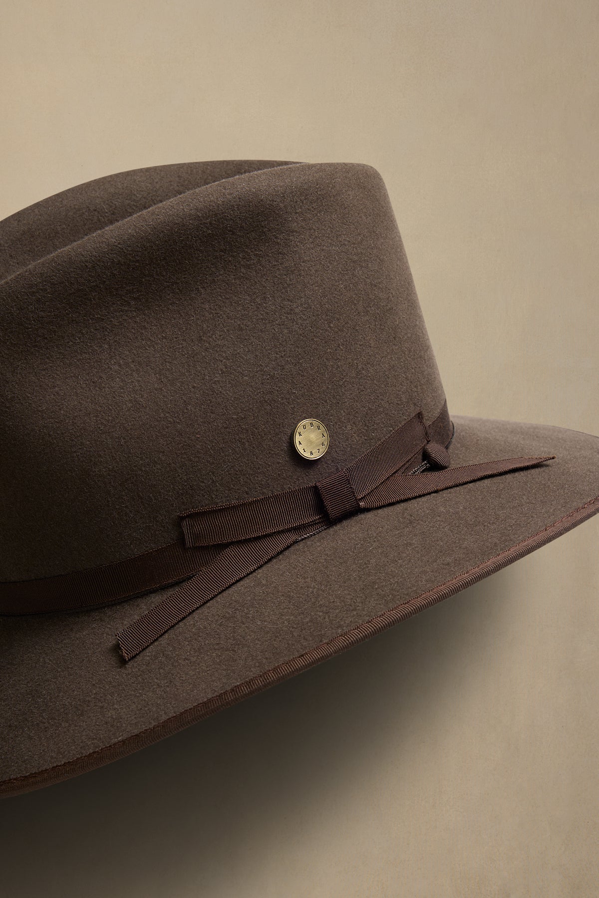 Brown fur felt cowboy hat with ribbon band and silver concho detail on neutral background