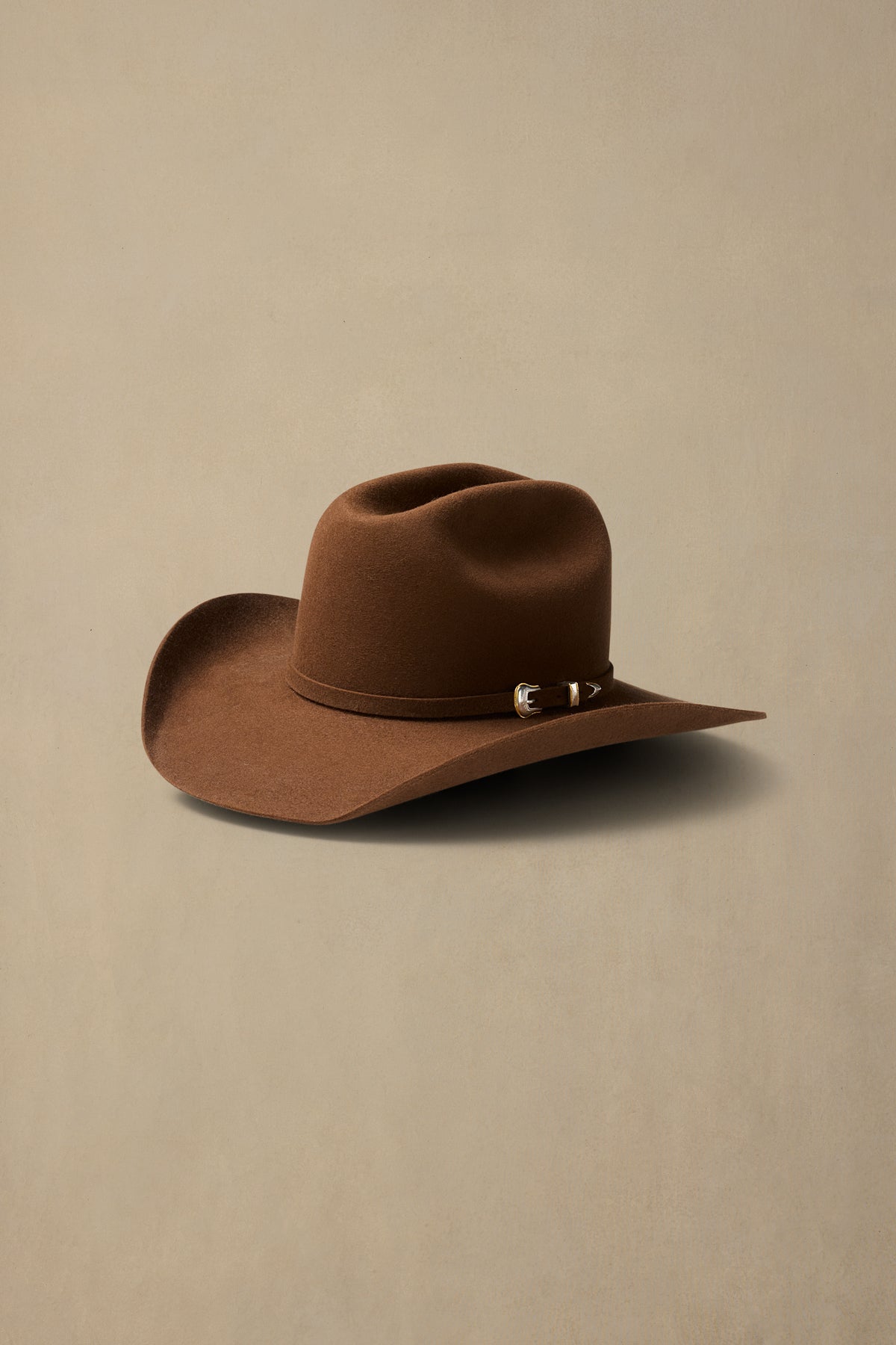 Brown rabbit fur cowboy hat with decorative band and wide brim on neutral background