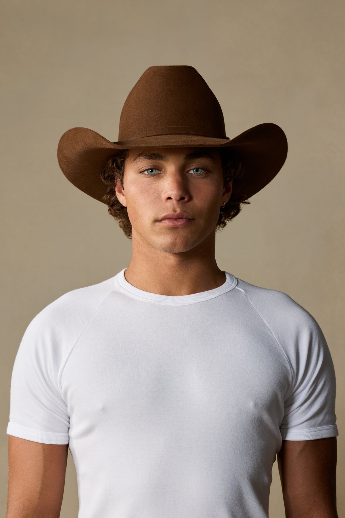 Brown fur felt cowboy hat with wide brim on man wearing white t-shirt against neutral background