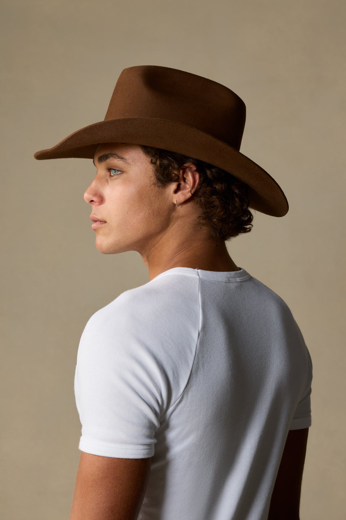 Man wearing brown felt cowboy hat with wide brim and white t-shirt, shown in profile against neutral background