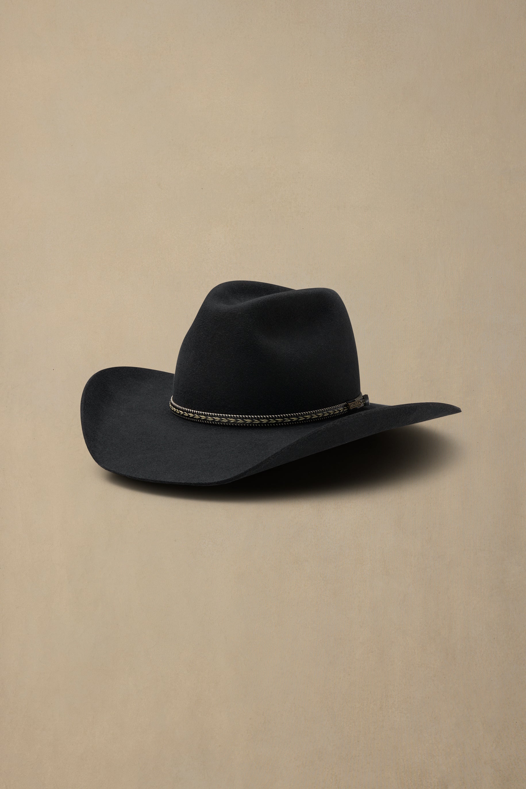 Black cowboy hat with decorative band on beige background, angled side view