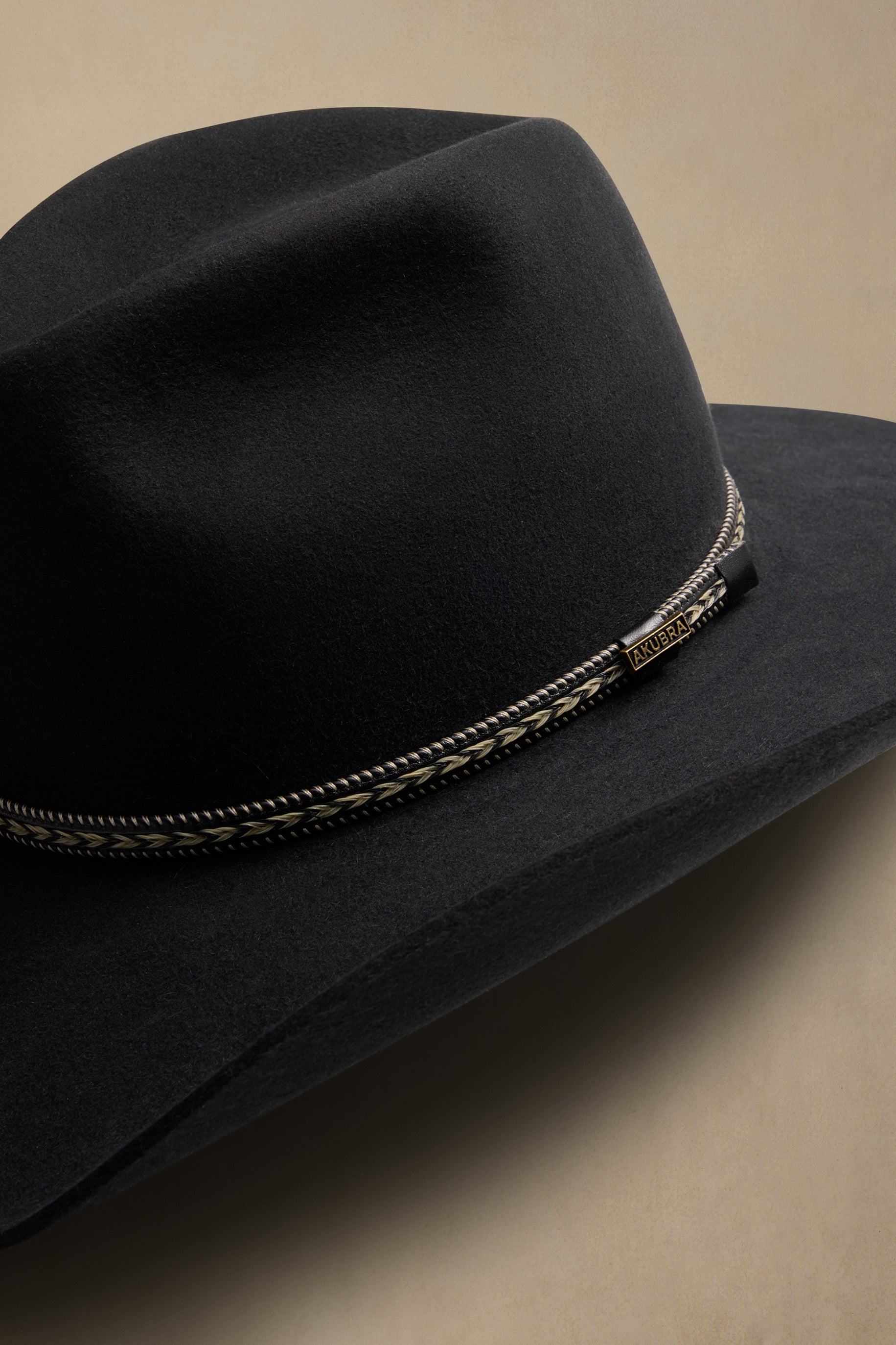 Black cowboy hat with decorative silver and gold braided band, angled side view on neutral background