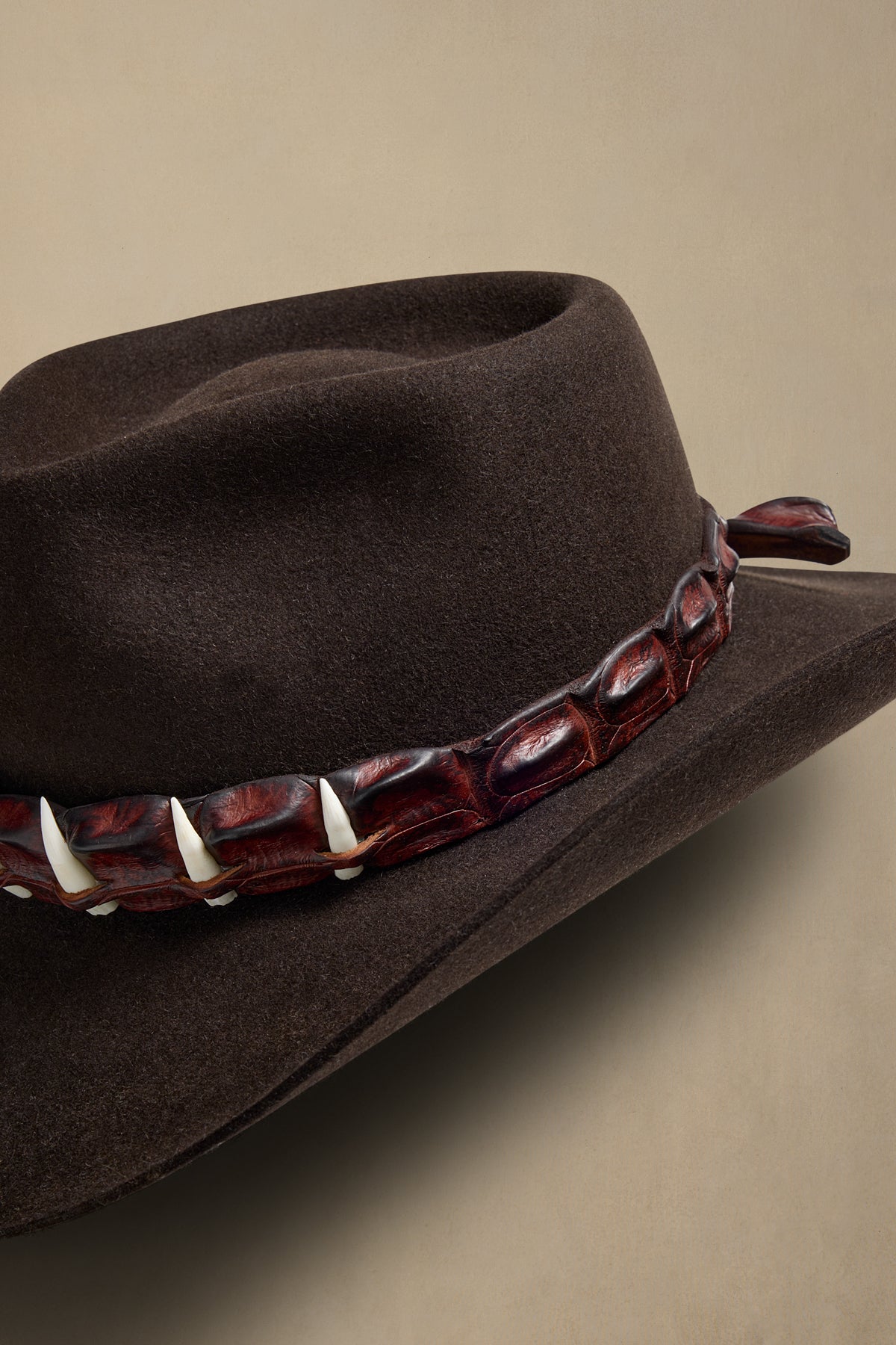 Charcoal felt cowboy hat with burgundy crocodile leather band and bone tooth accents, angled side view