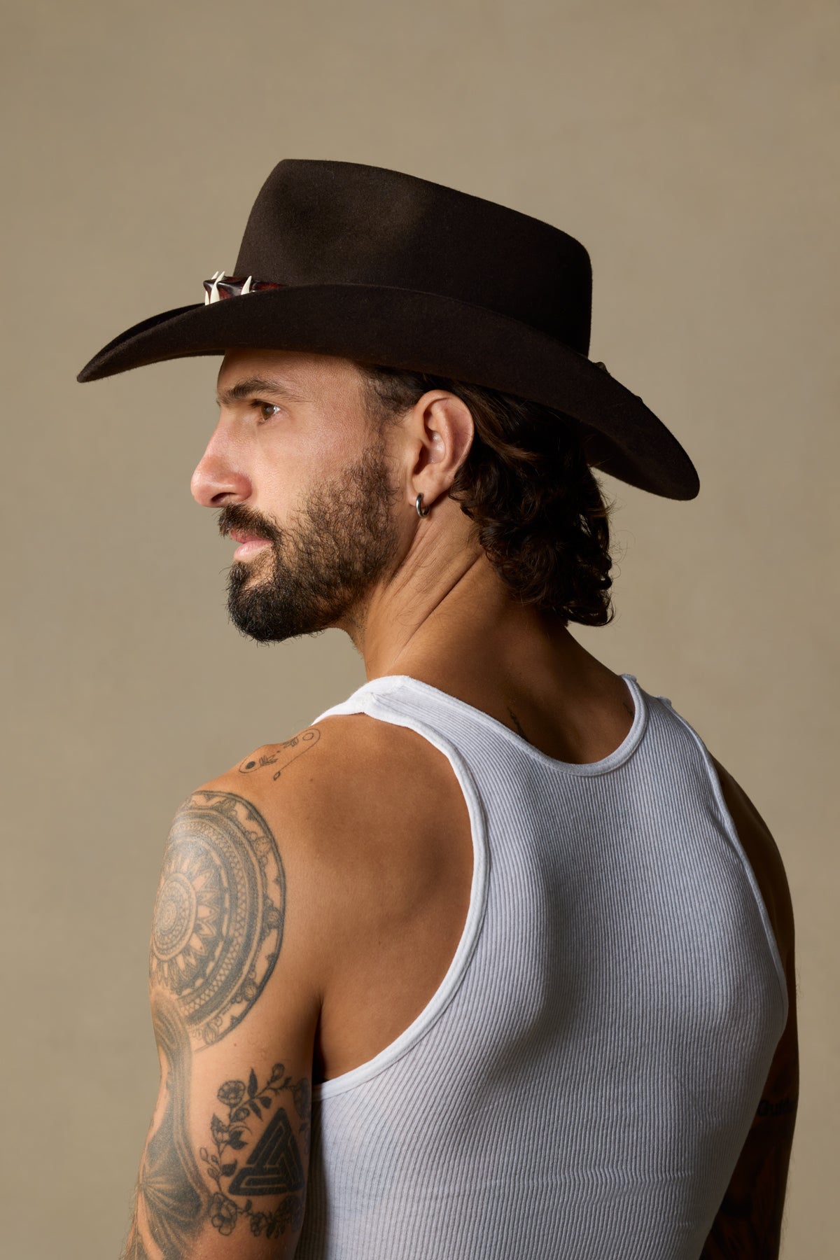 Black cowboy hat with silver studs worn by man with dark hair and beard against neutral background