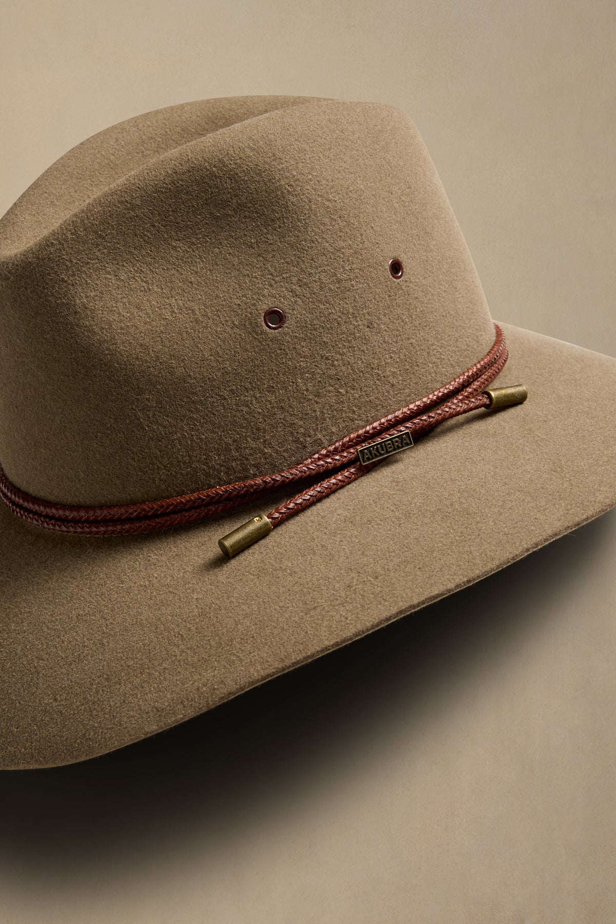 Tan rabbit fur Traveller hat with burgundy braided cord band and brass accents, angled side view