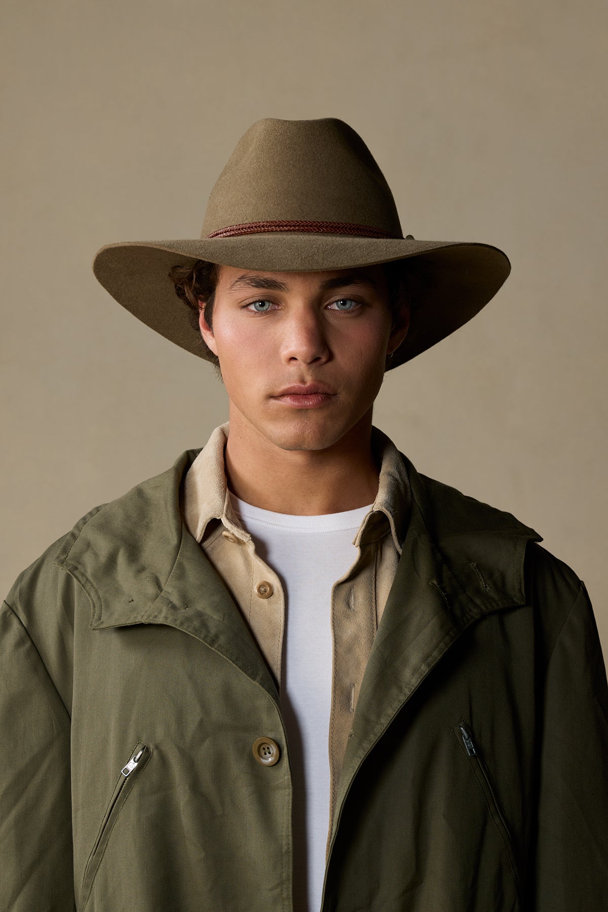 Tan rabbit fur traveller hat with burgundy band on model wearing olive jacket against neutral background