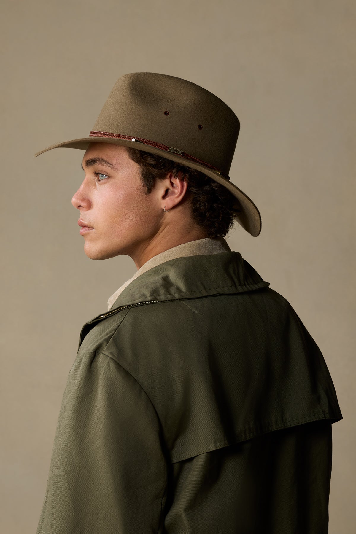 Man wearing tan rabbit fur traveller hat with burgundy band, shown in profile against neutral background