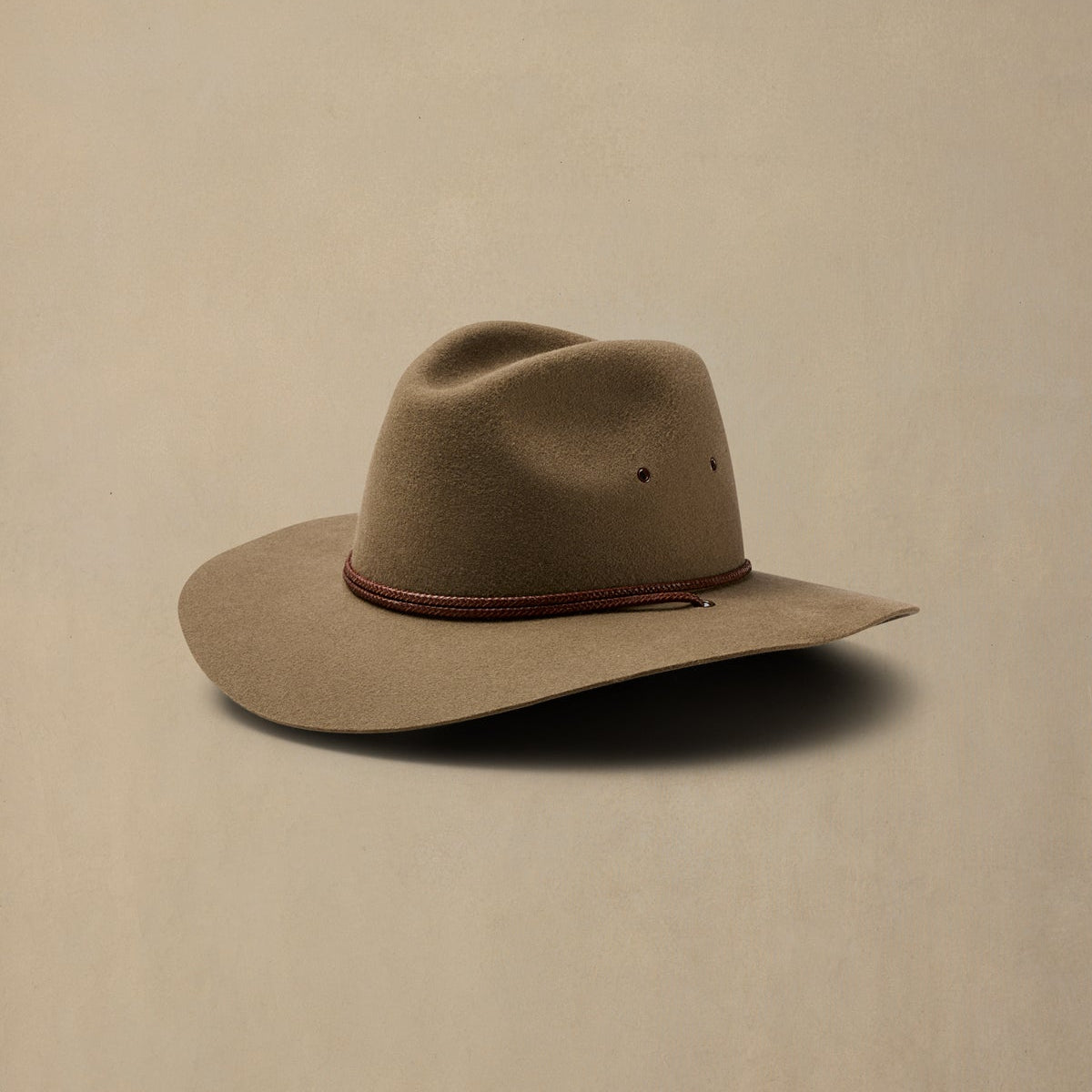 Tan rabbit fur felt cowboy hat with burgundy cord band on neutral background