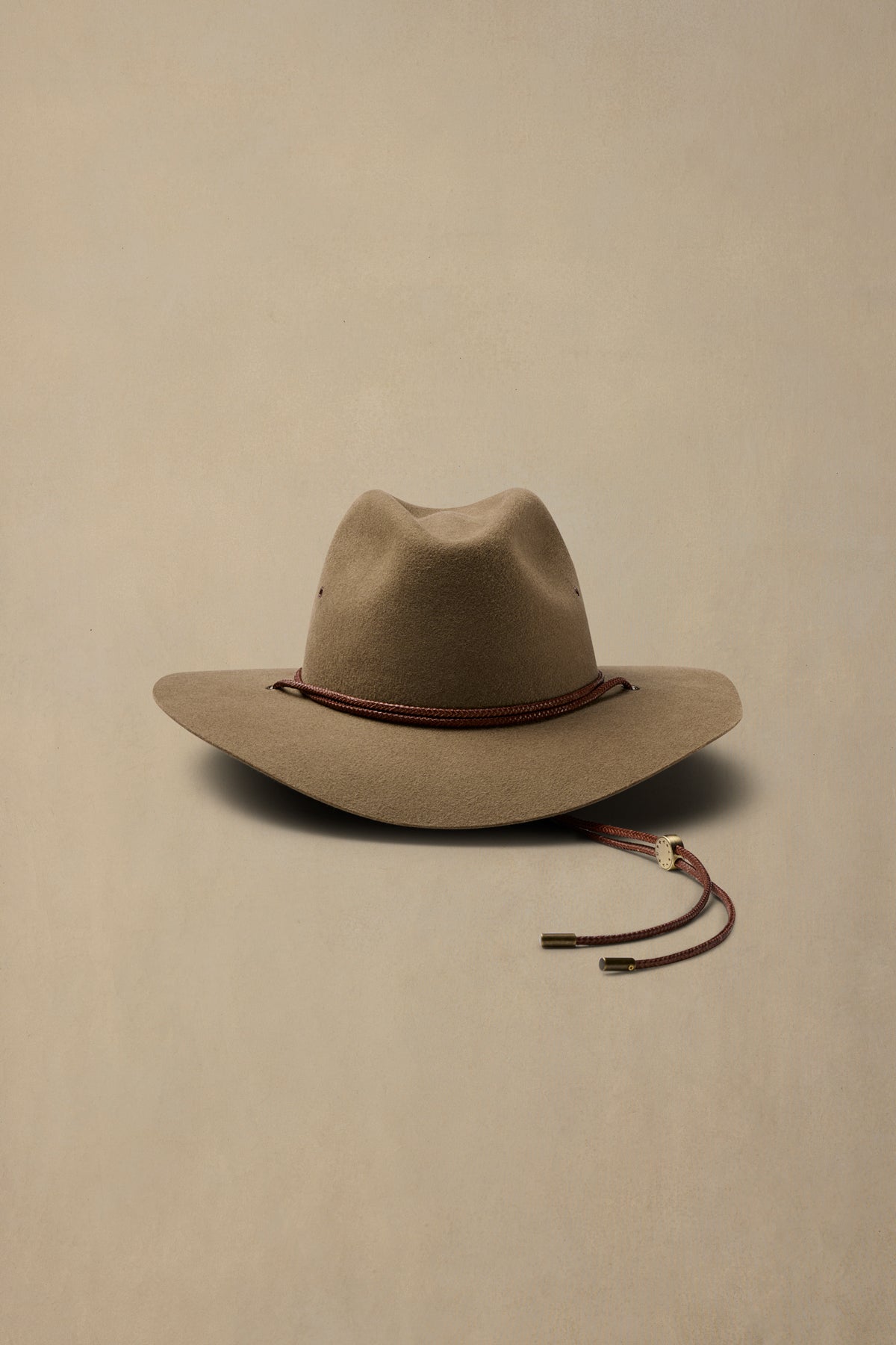 Tan rabbit fur cowboy hat with burgundy cord band and chin strap on neutral beige background