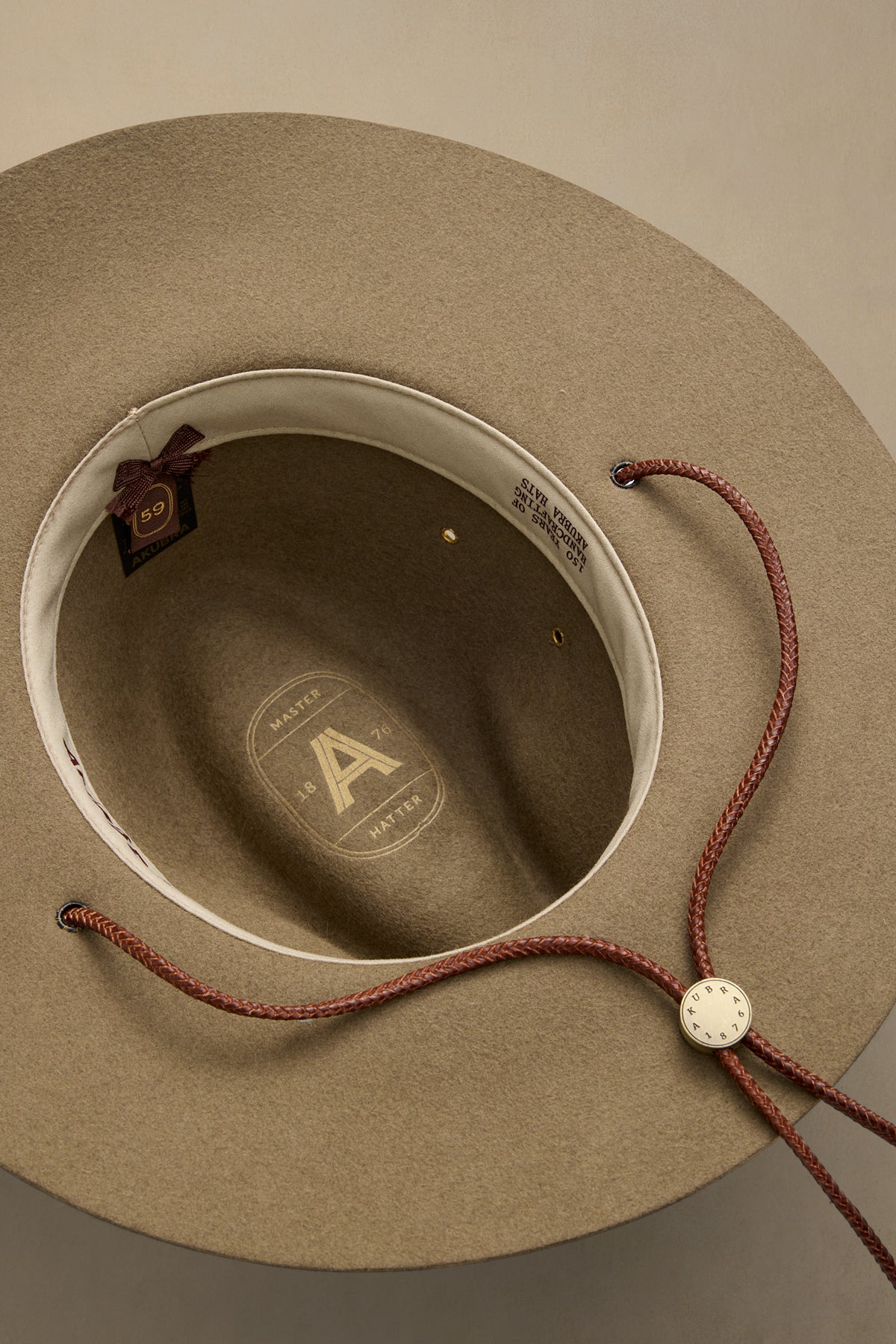 Tan rabbit fur traveller hat displayed from above showing interior branding and burgundy chin cord with toggle closure