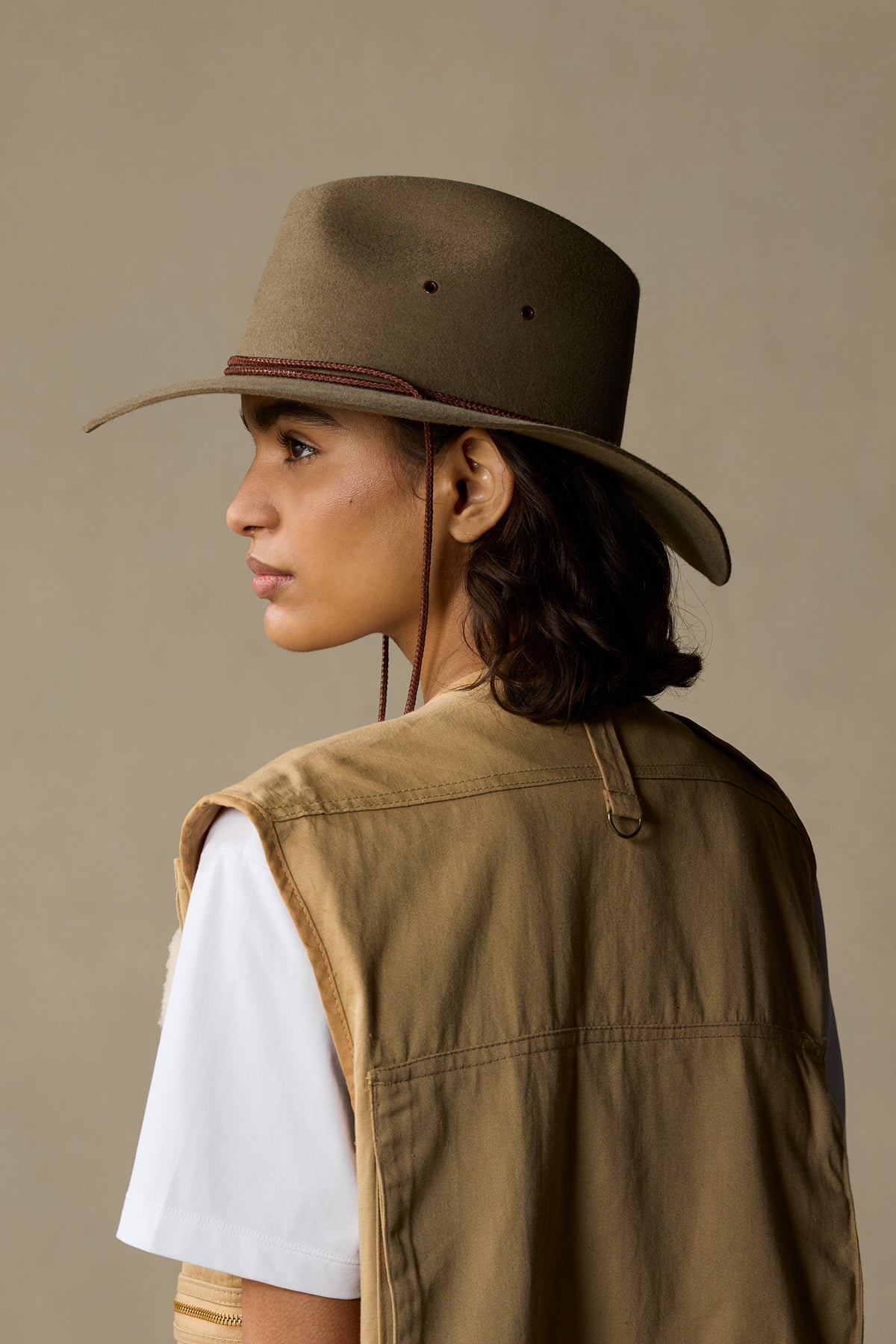 Woman wearing tan rabbit fur traveller hat with burgundy band, viewed from side profile against neutral background