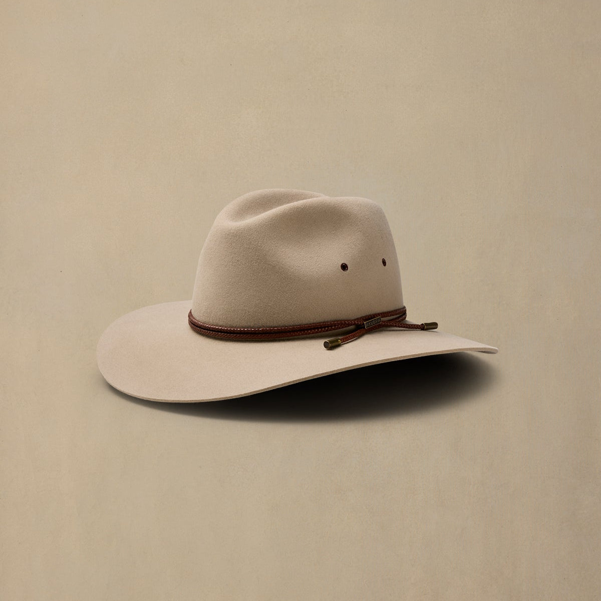 Cream-colored rabbit fur felt cowboy hat with brown braided band, displayed against beige background