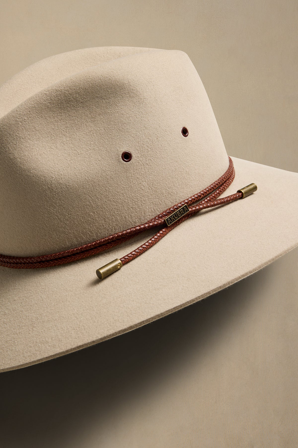 Cream felt cowboy hat with burgundy braided band and brass accents, angled side view