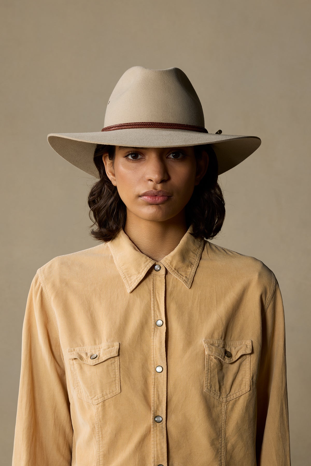 Sand-colored traveller hat with wide brim worn by woman in tan corduroy shirt against neutral background