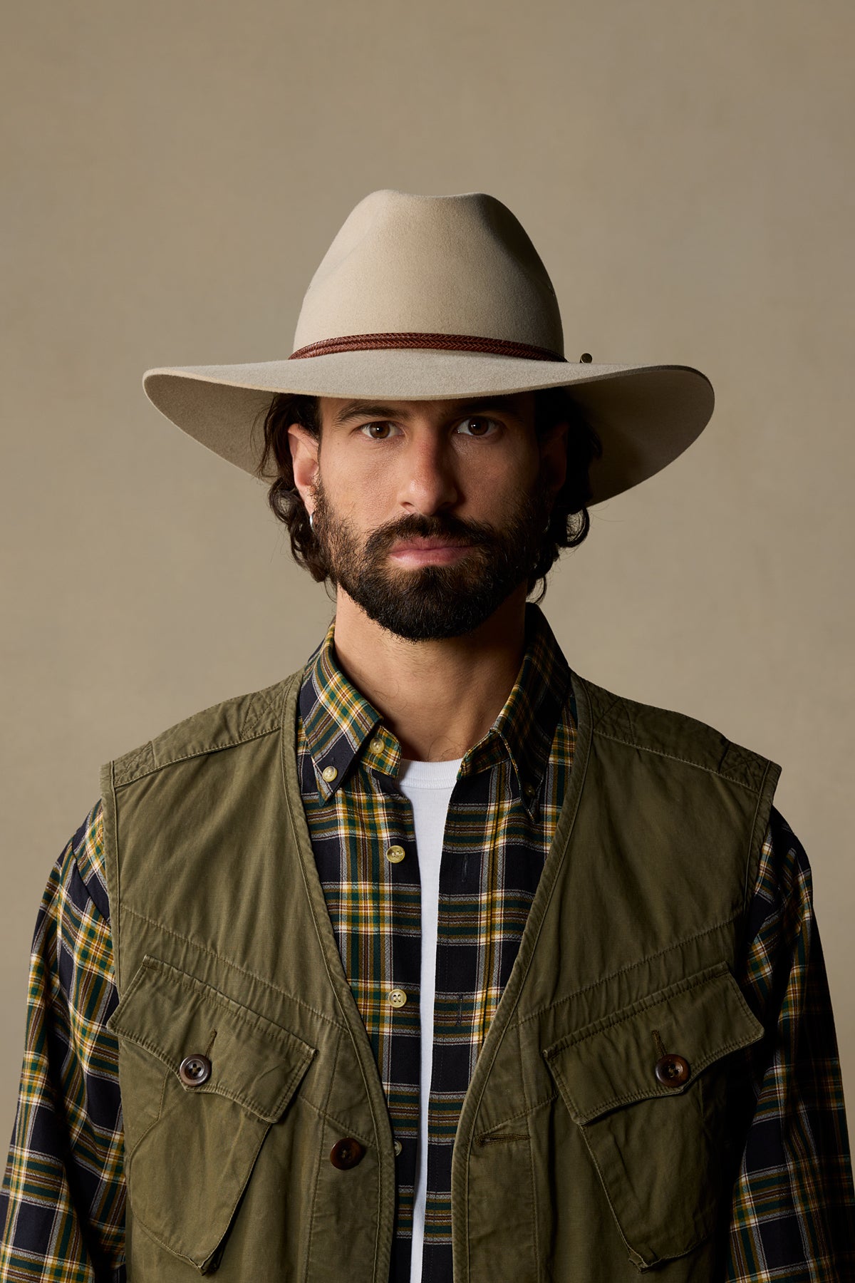 Bearded man wearing cream Traveller hat with brown band and olive quilted vest over plaid shirt