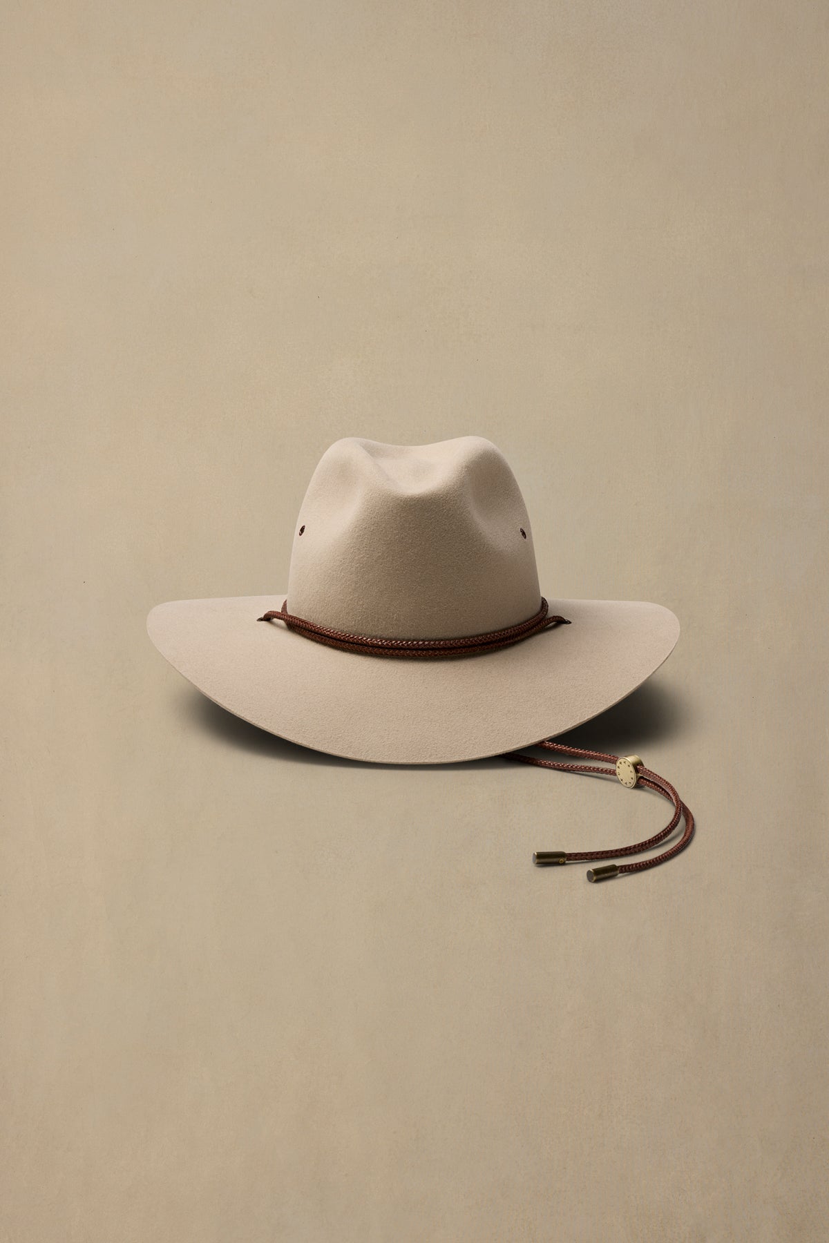 Cream rabbit fur felt cowboy hat with brown braided chin strap on beige background