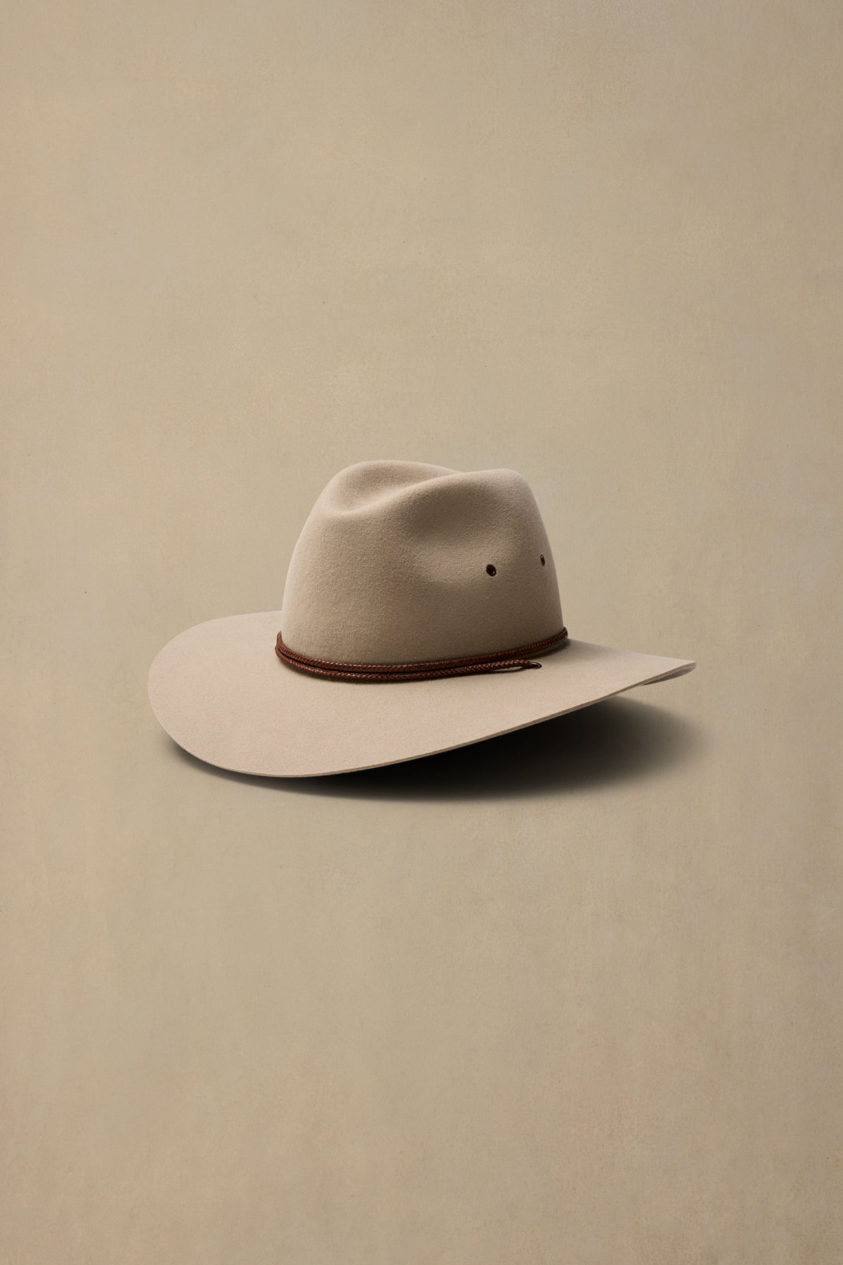 Cream-colored rabbit fur felt cowboy hat with brown braided band, displayed on neutral beige background
