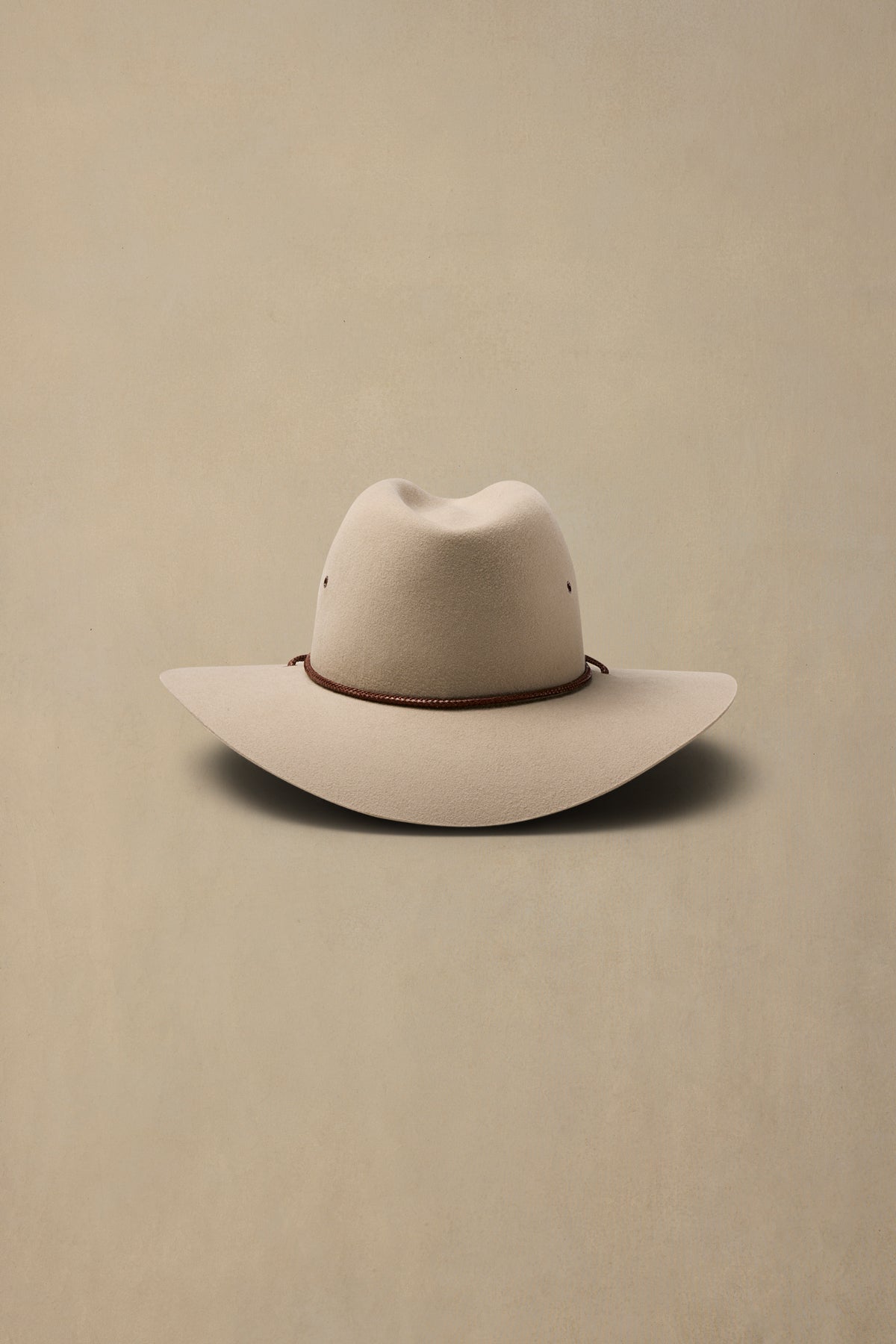 Cream-colored rabbit fur felt cowboy hat with brown chin cord on neutral beige background