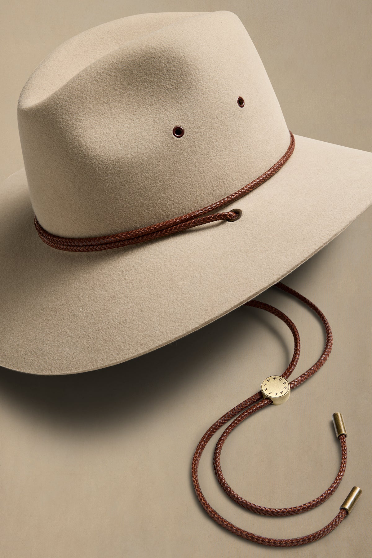 Cream rabbit fur cowboy hat with brown braided cord and chin strap on beige background