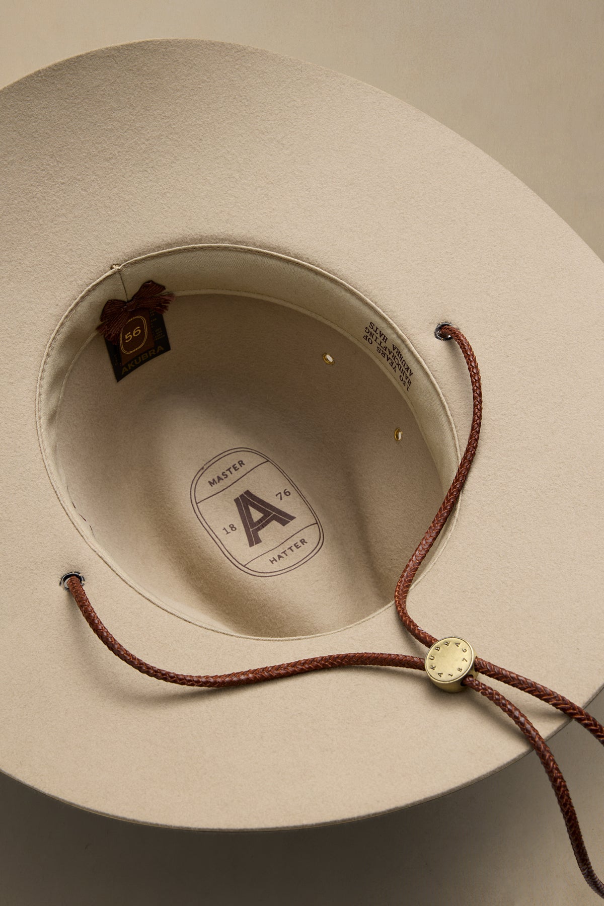 Cream felt cowboy hat interior view showing Master Hatter label, burgundy chin strap with metal clasp, and brown fabric tag
