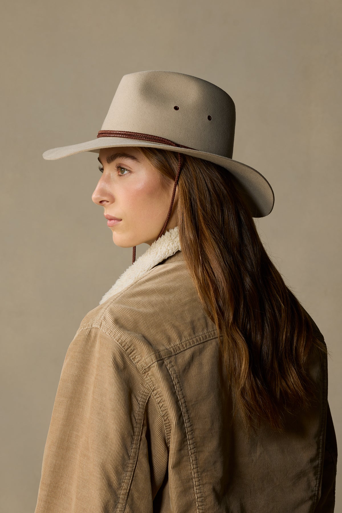 Woman wearing sand-colored rabbit fur felt traveller hat with chin strap, shown in profile view