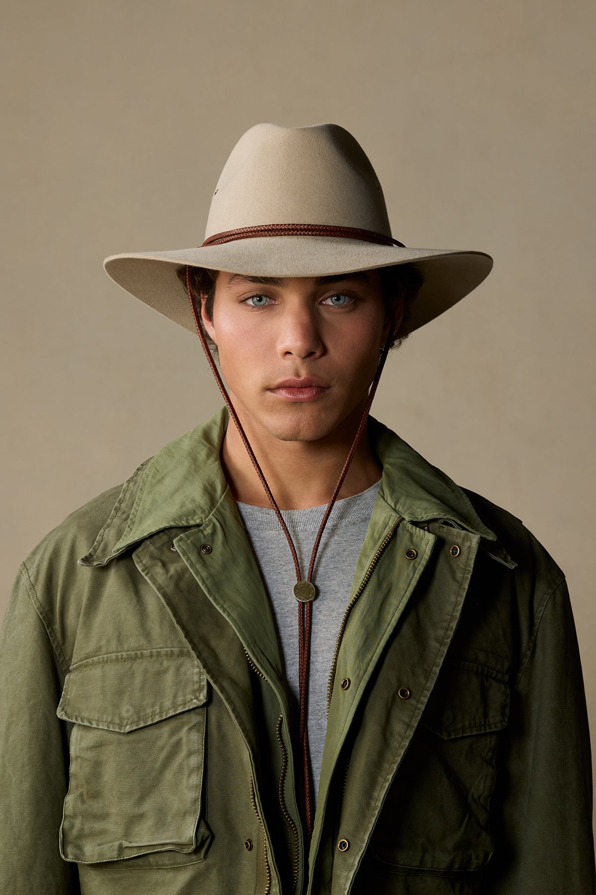 Sand-colored fur felt cowboy hat with brown chin strap on male model wearing green jacket