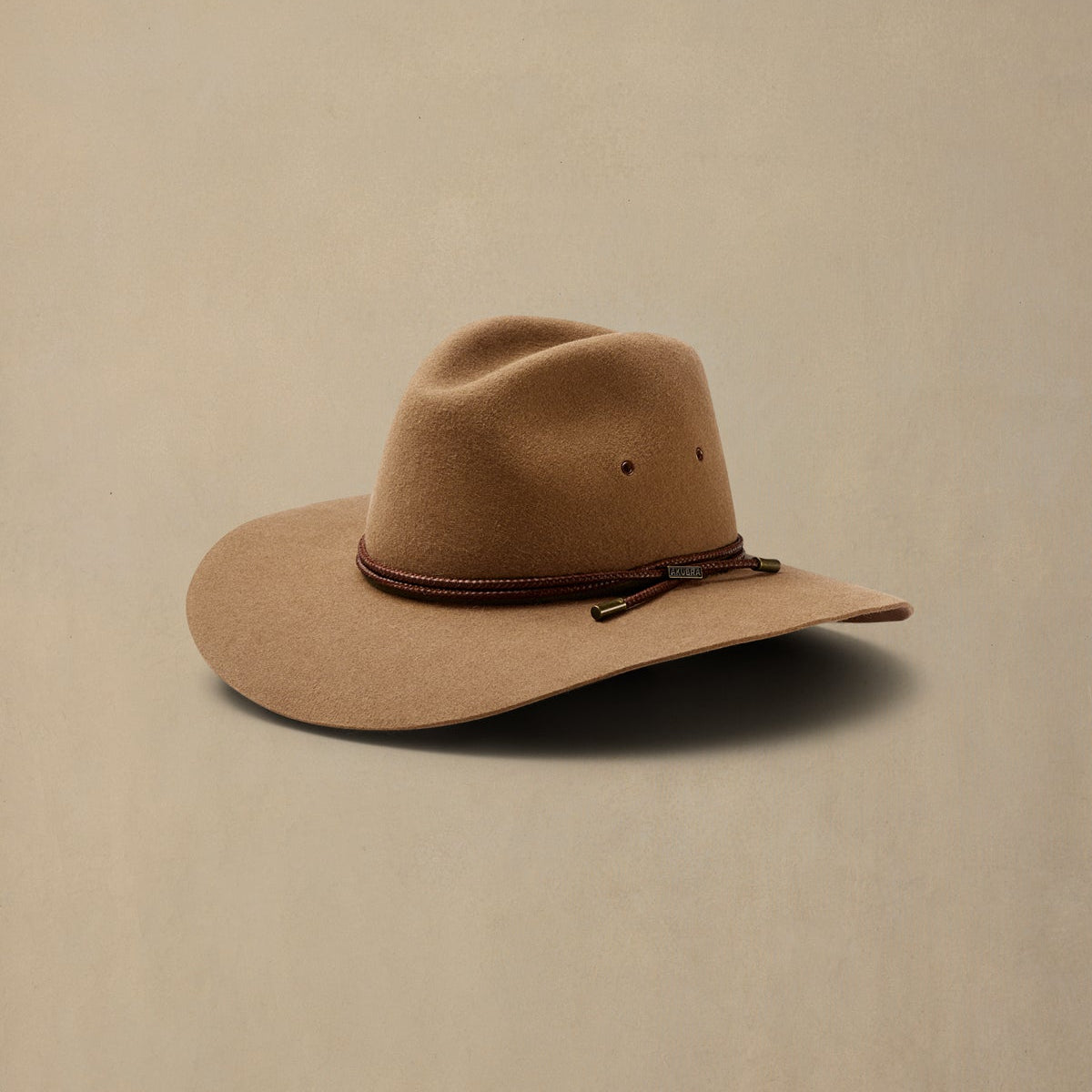 Tan rabbit fur cowboy hat with brown cord band, displayed against neutral beige background
