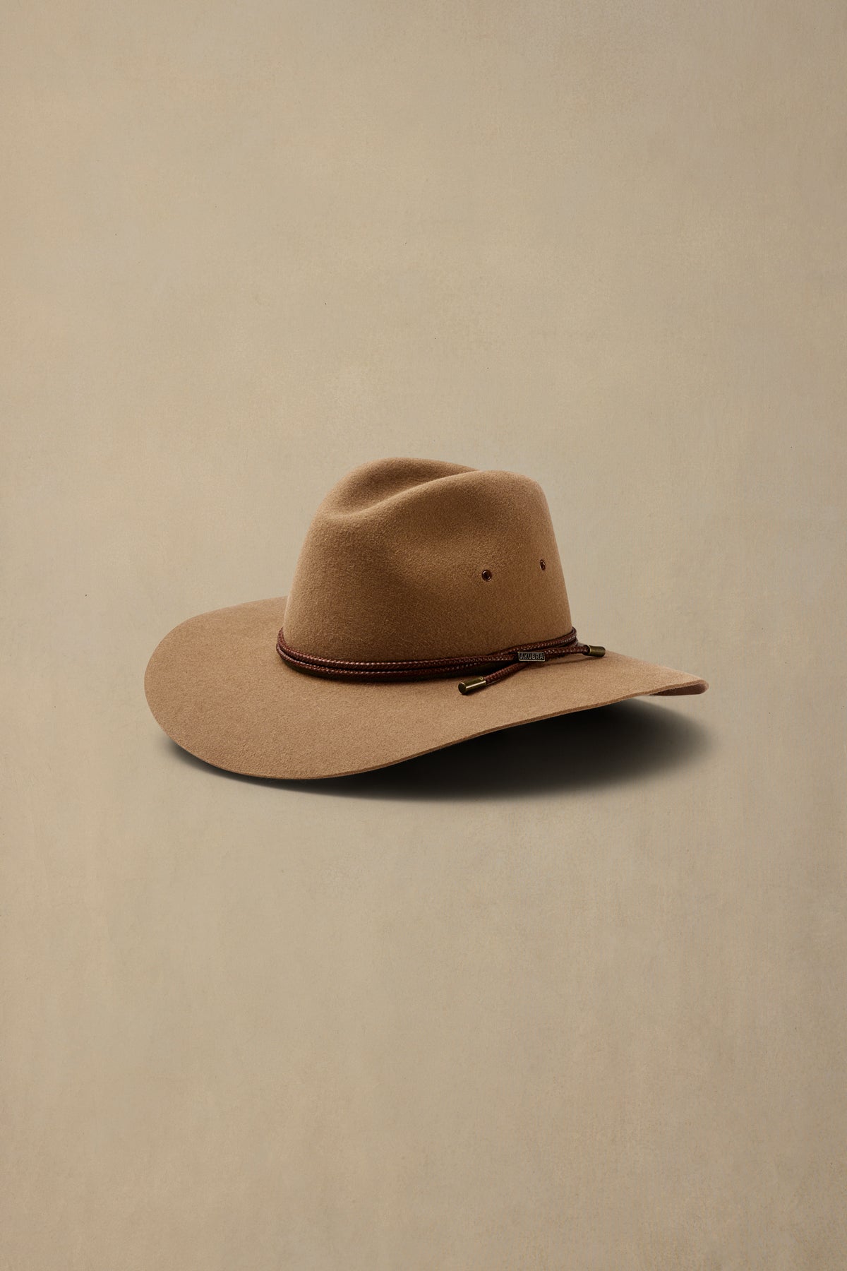 Tan rabbit fur cowboy hat with brown rope band on neutral background
