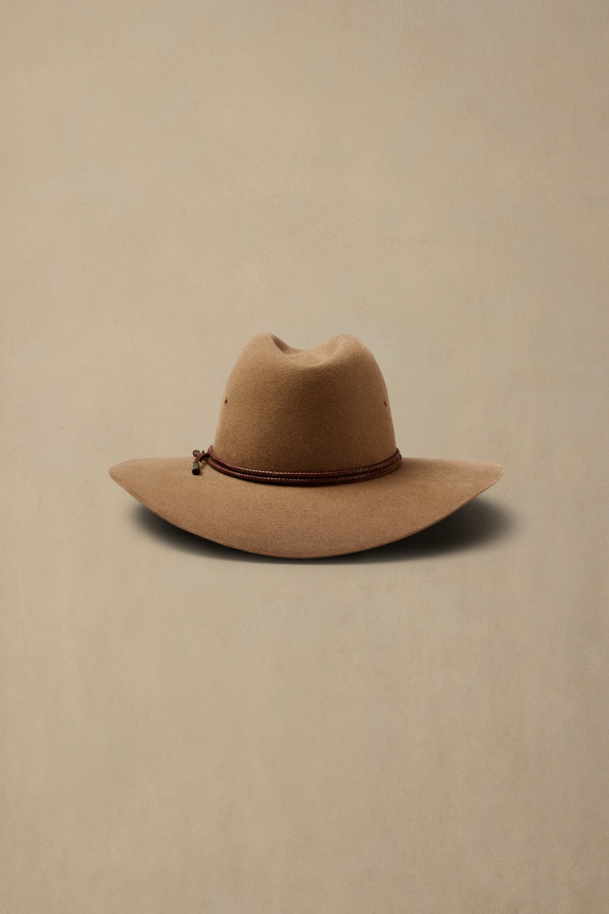 Tan rabbit fur cowboy hat with brown beaded band on neutral background