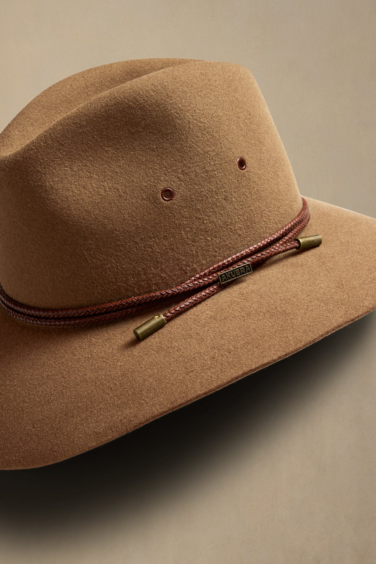 Tan rabbit fur cowboy hat with burgundy braided chin strap and brass accents, angled view