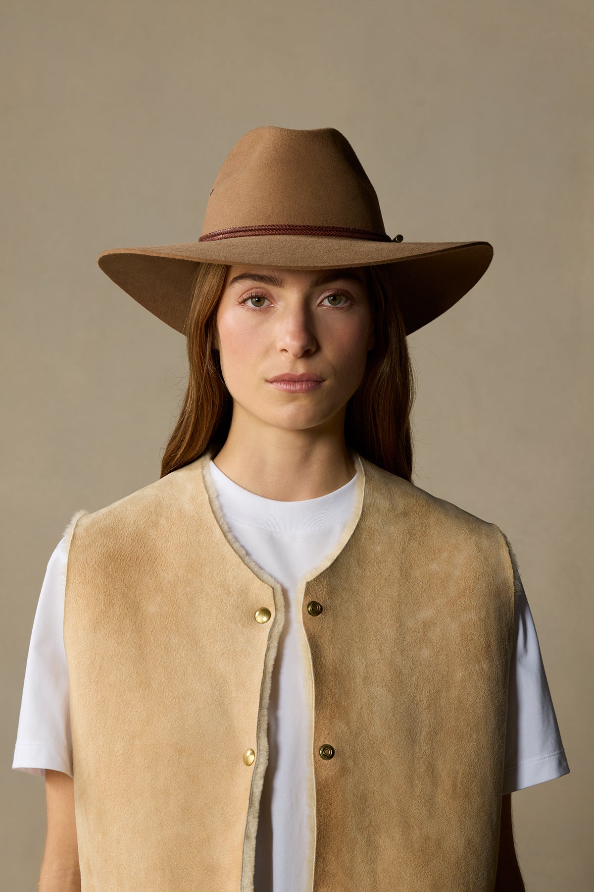 Tan rabbit fur cowboy hat with burgundy band on model wearing cream vest and white shirt against neutral background