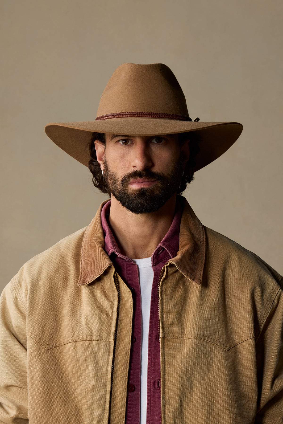 Tan rabbit fur Traveller hat with burgundy band on bearded man wearing camel jacket against neutral background