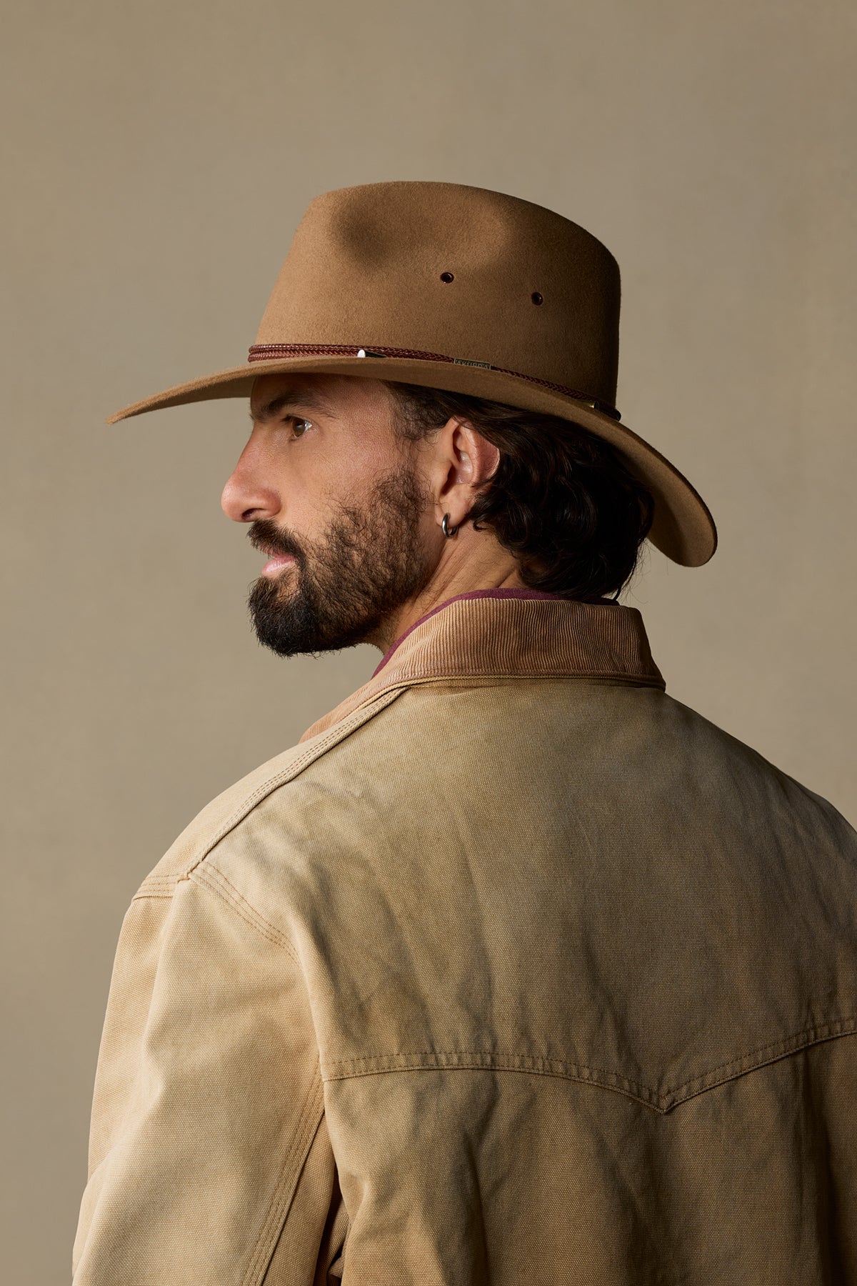 Man wearing tan rabbit fur cowboy hat with burgundy band, side profile view against neutral background