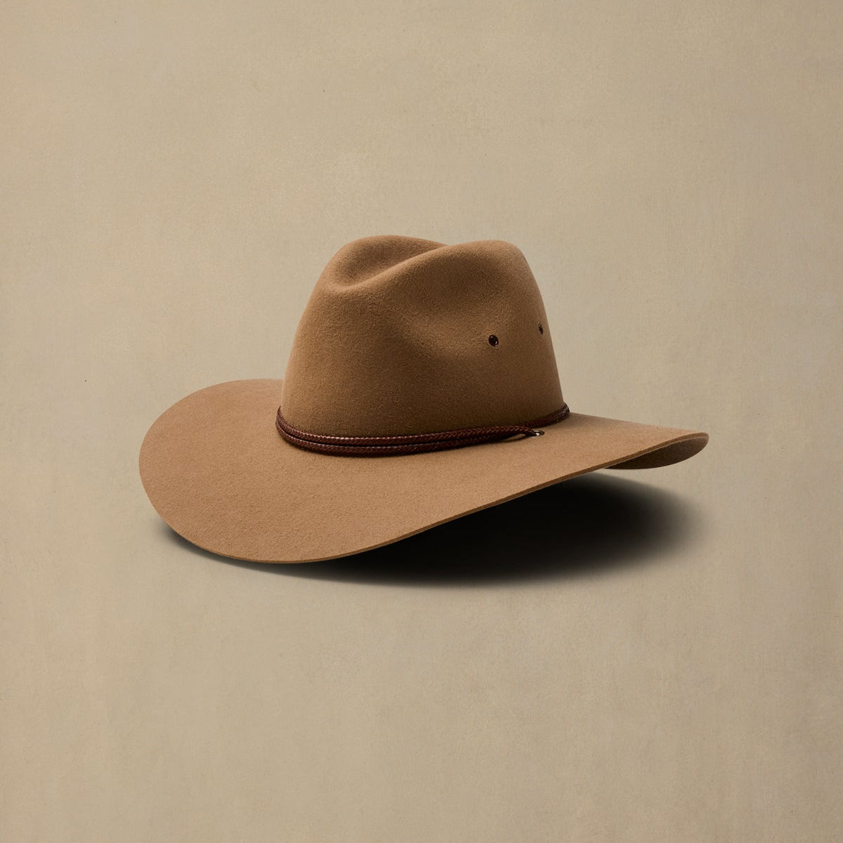 Tan rabbit fur cowboy hat with brown cord band, displayed against neutral beige background
