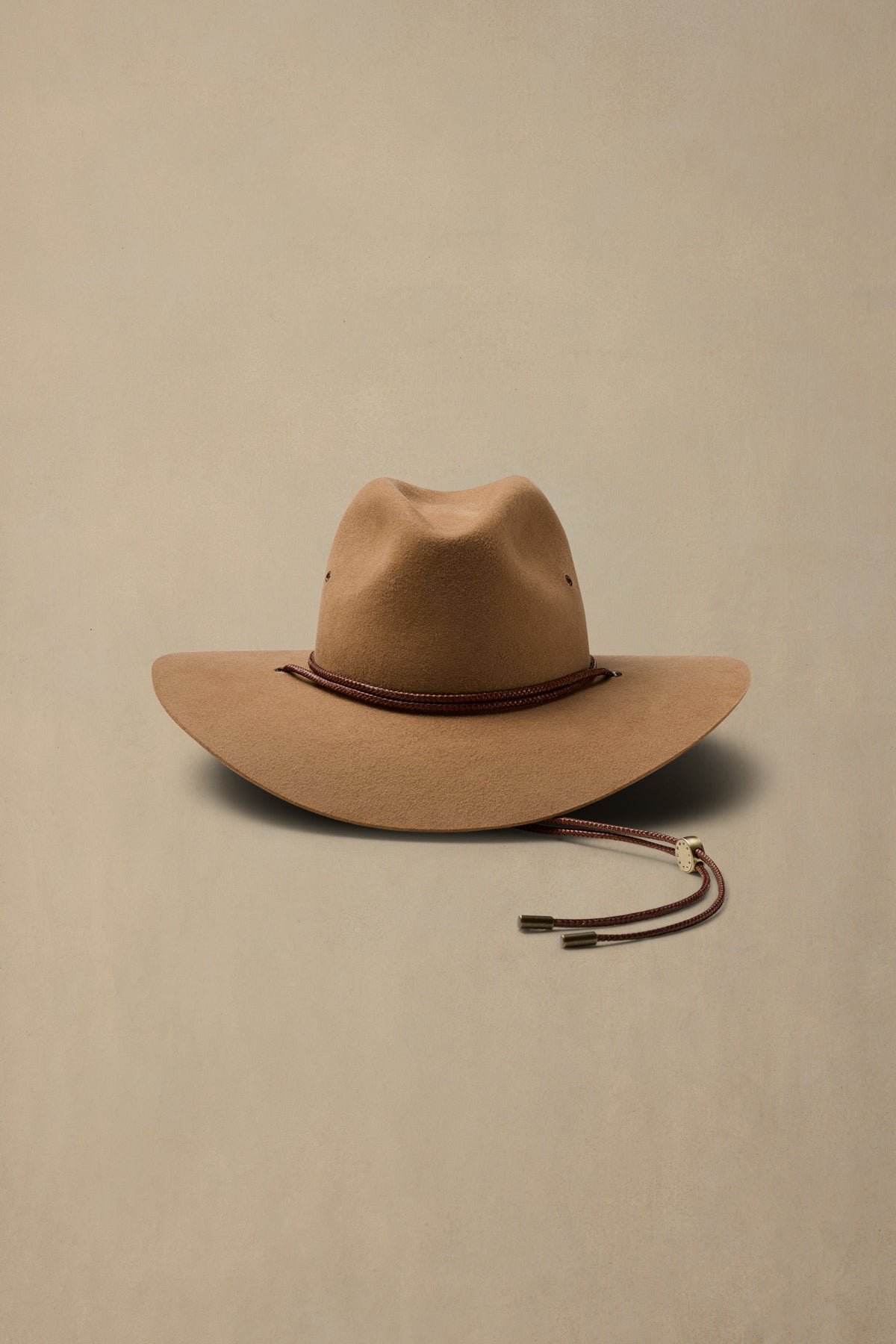 Tan rabbit fur cowboy hat with burgundy chin strap on neutral background