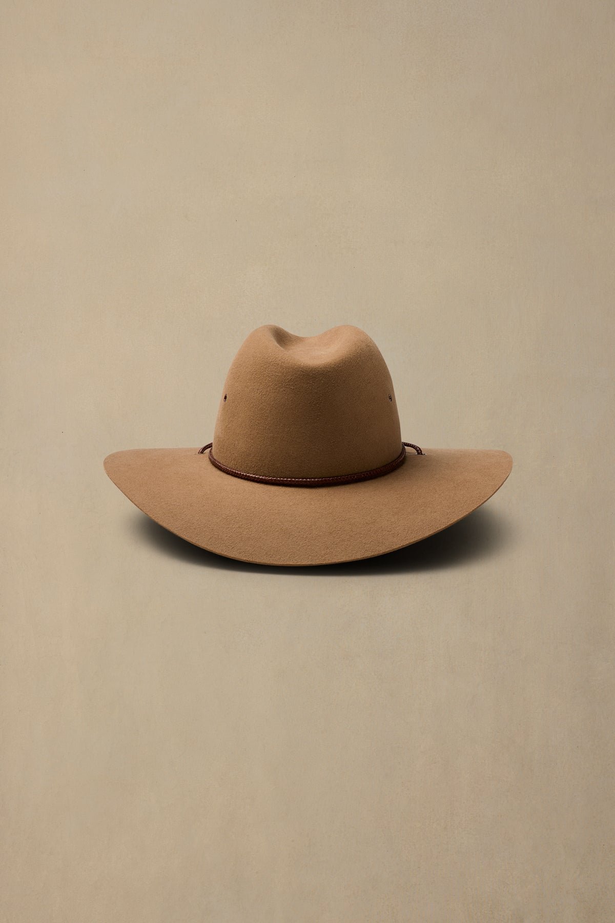 Tan rabbit fur cowboy hat with brown chin strap on neutral beige background