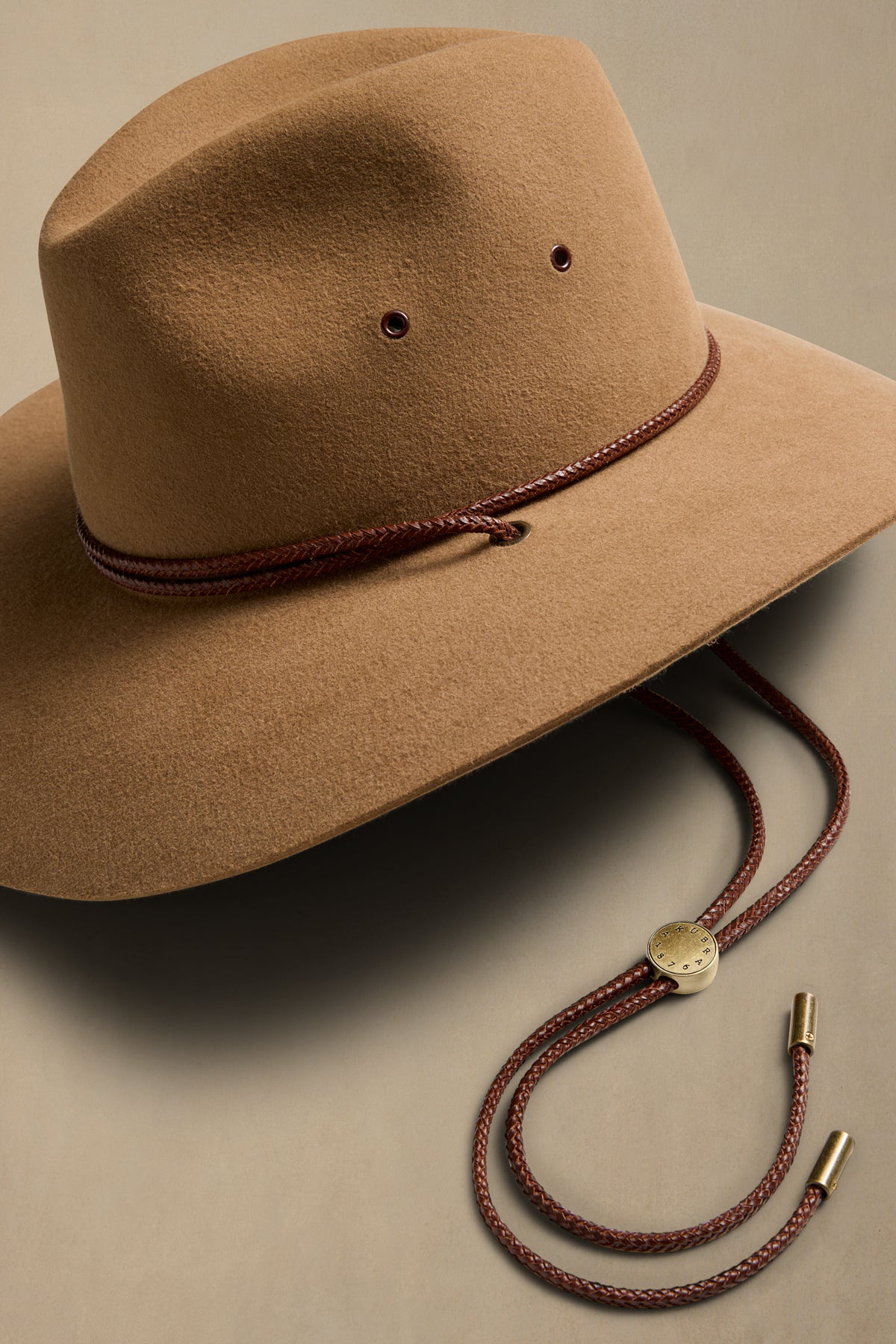 Tan rabbit fur cowboy hat with burgundy cord and chin strap detail on neutral background