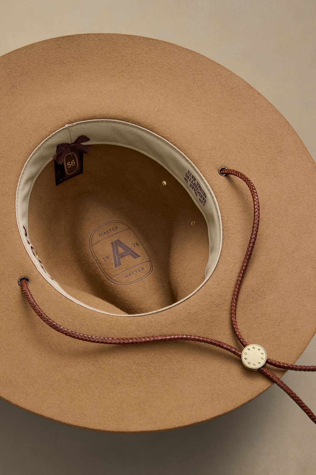 Tan rabbit fur traveler hat interior view showing cream-colored sweatband with size tag and braided chin strap with metal button