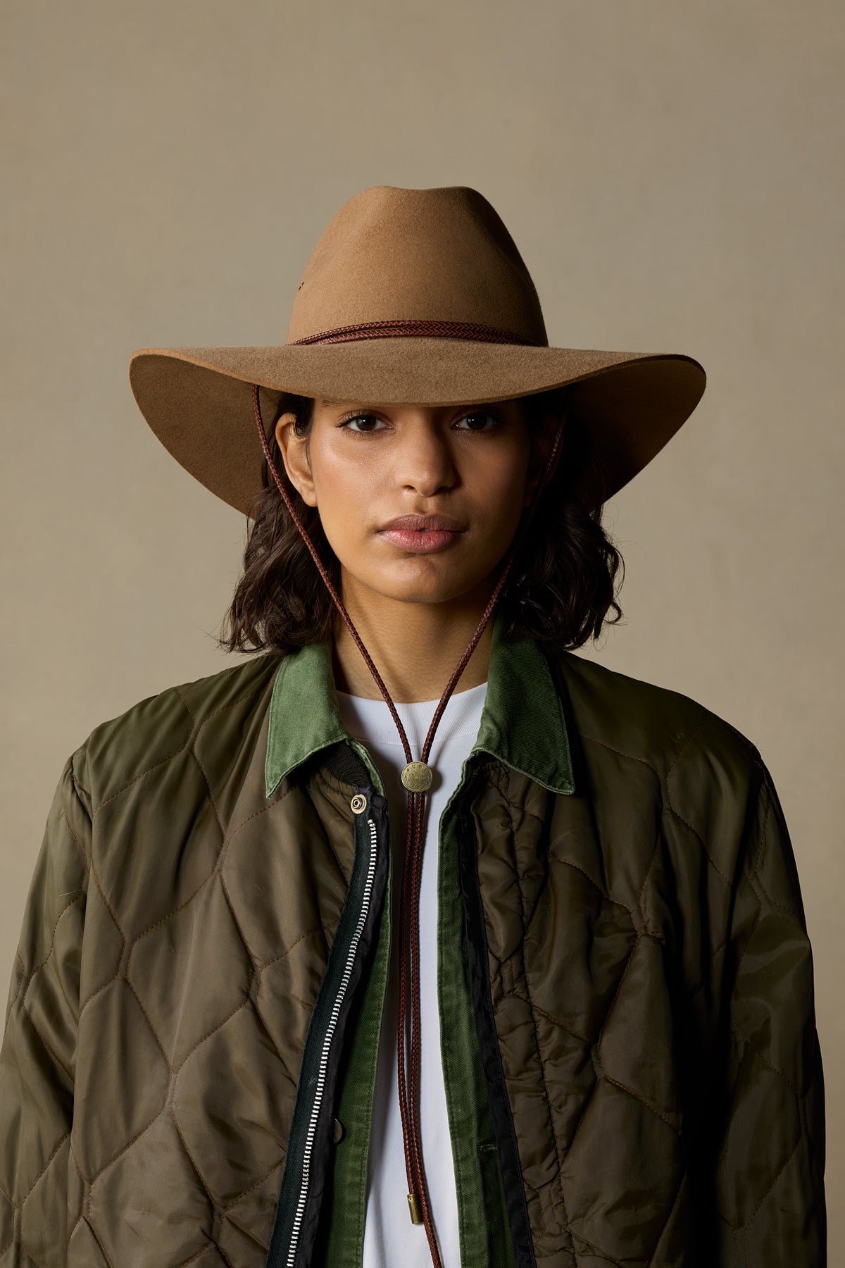 Tan rabbit fur cowboy hat with braided band, styled with olive quilted jacket on neutral background
