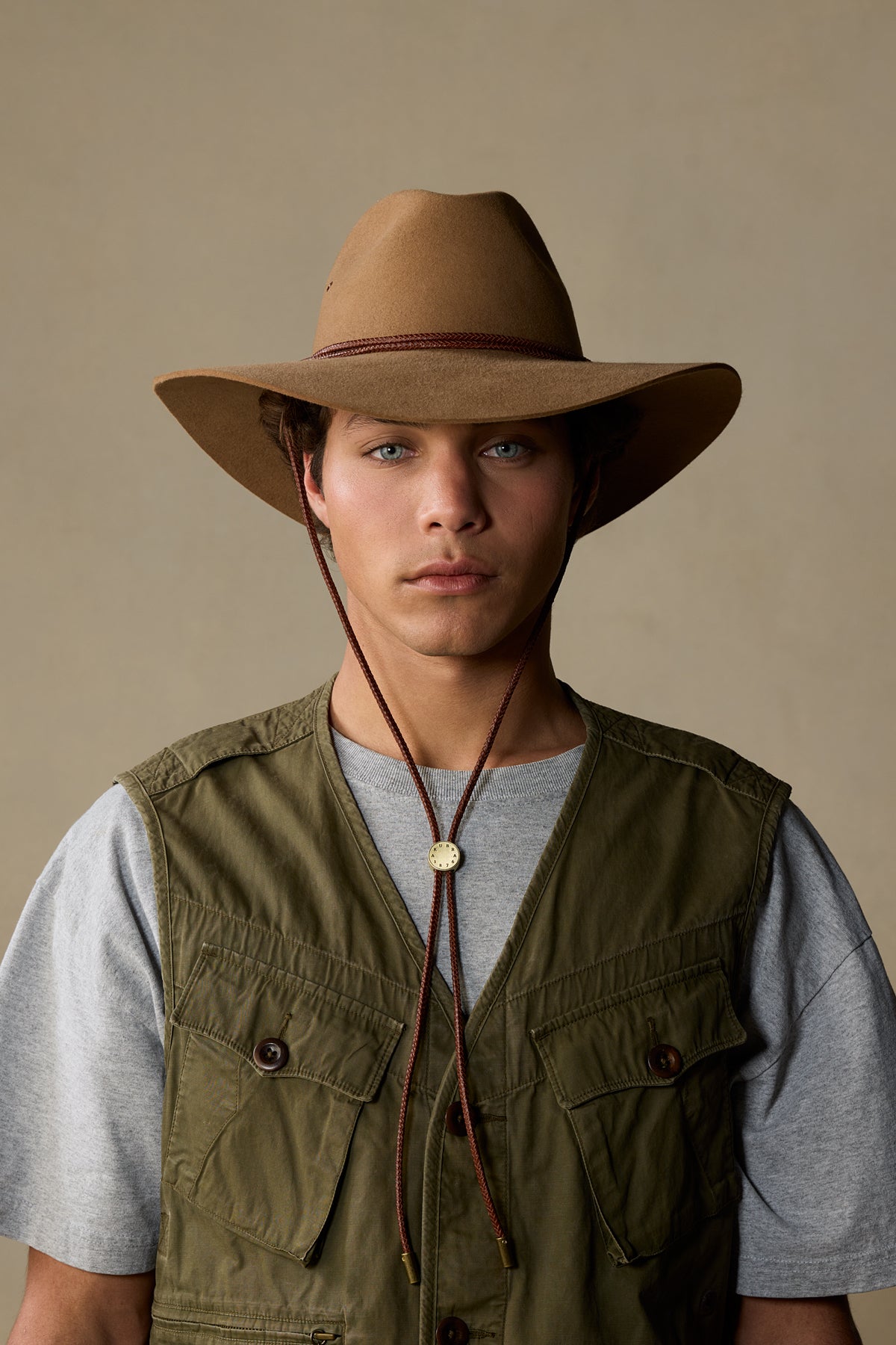 Tan fur felt cowboy hat with burgundy chin strap worn by man in olive vest