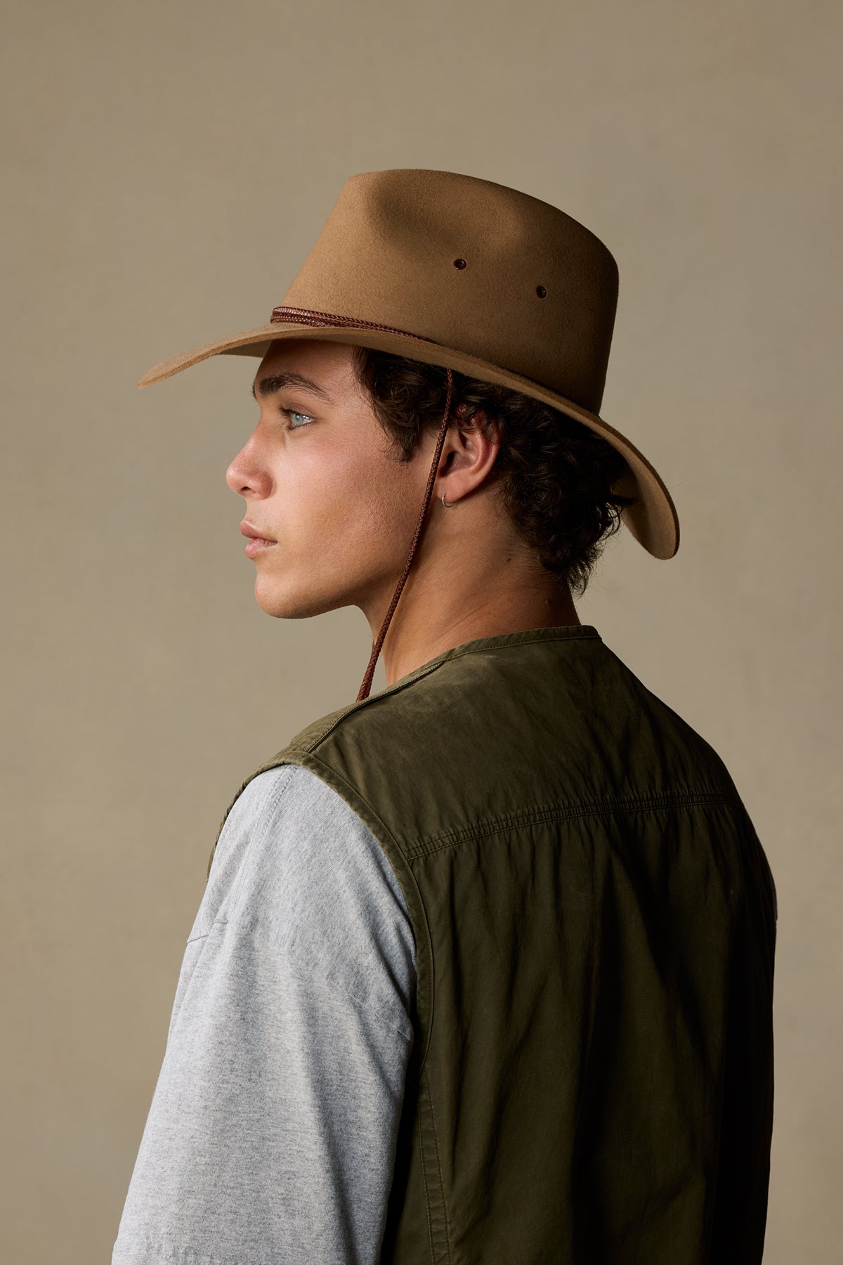 Tan rabbit fur cowboy hat with chin strap worn by person in profile against neutral background