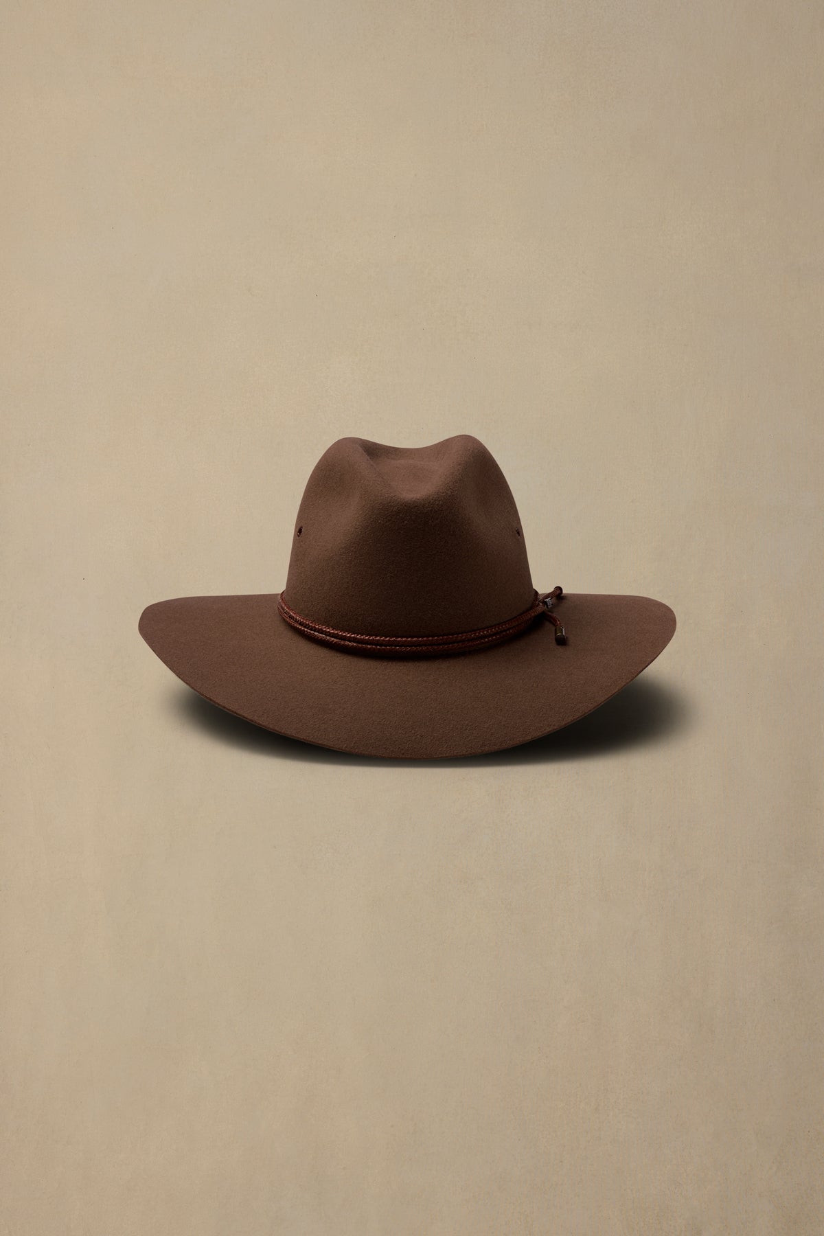 Brown rabbit fur cowboy hat with braided band detail on cream background